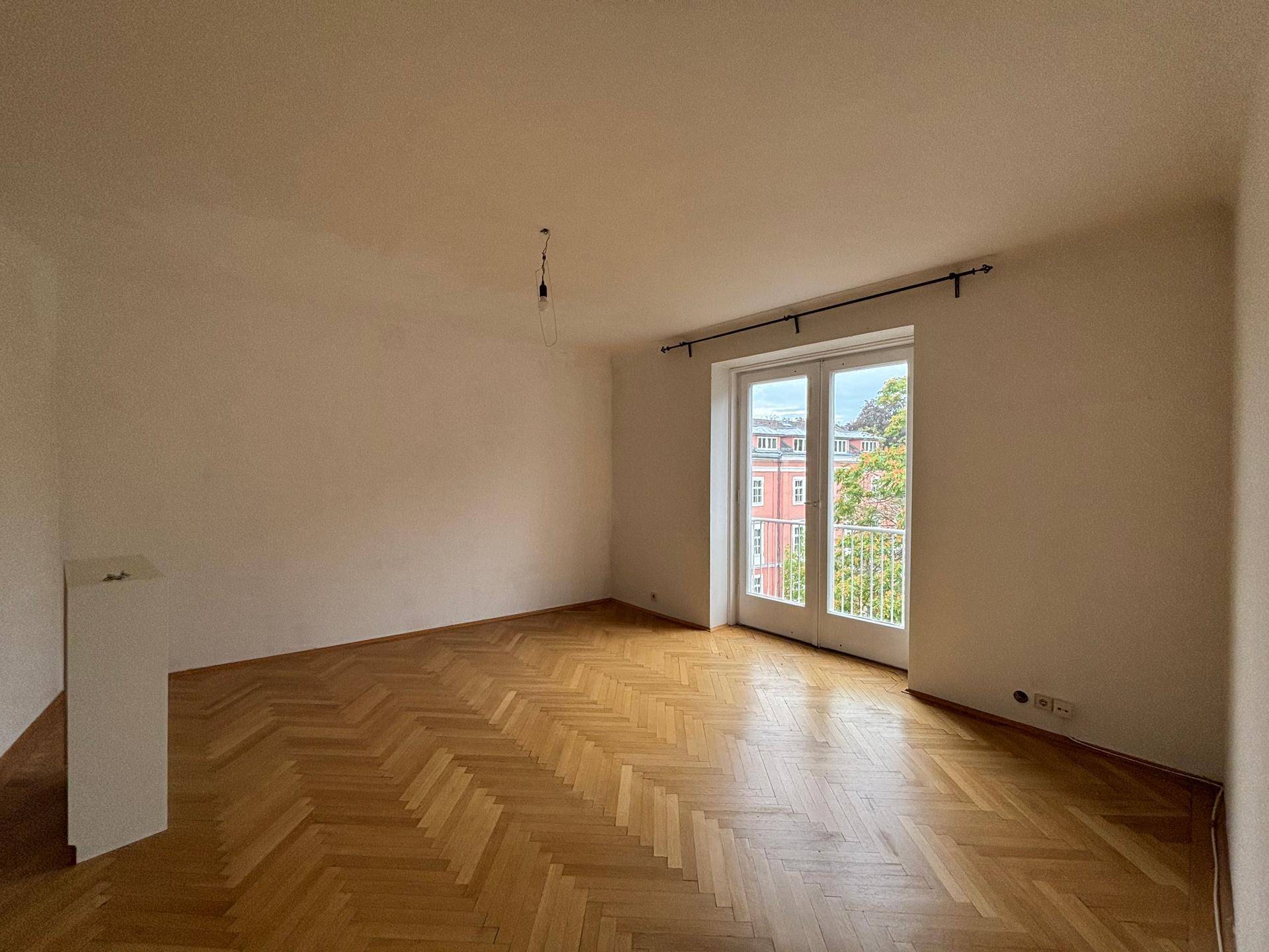 Lichtdurchflutetes Zimmer mit Fischgrätparkett und französischem Balkon, ideal für Wohnzwecke.