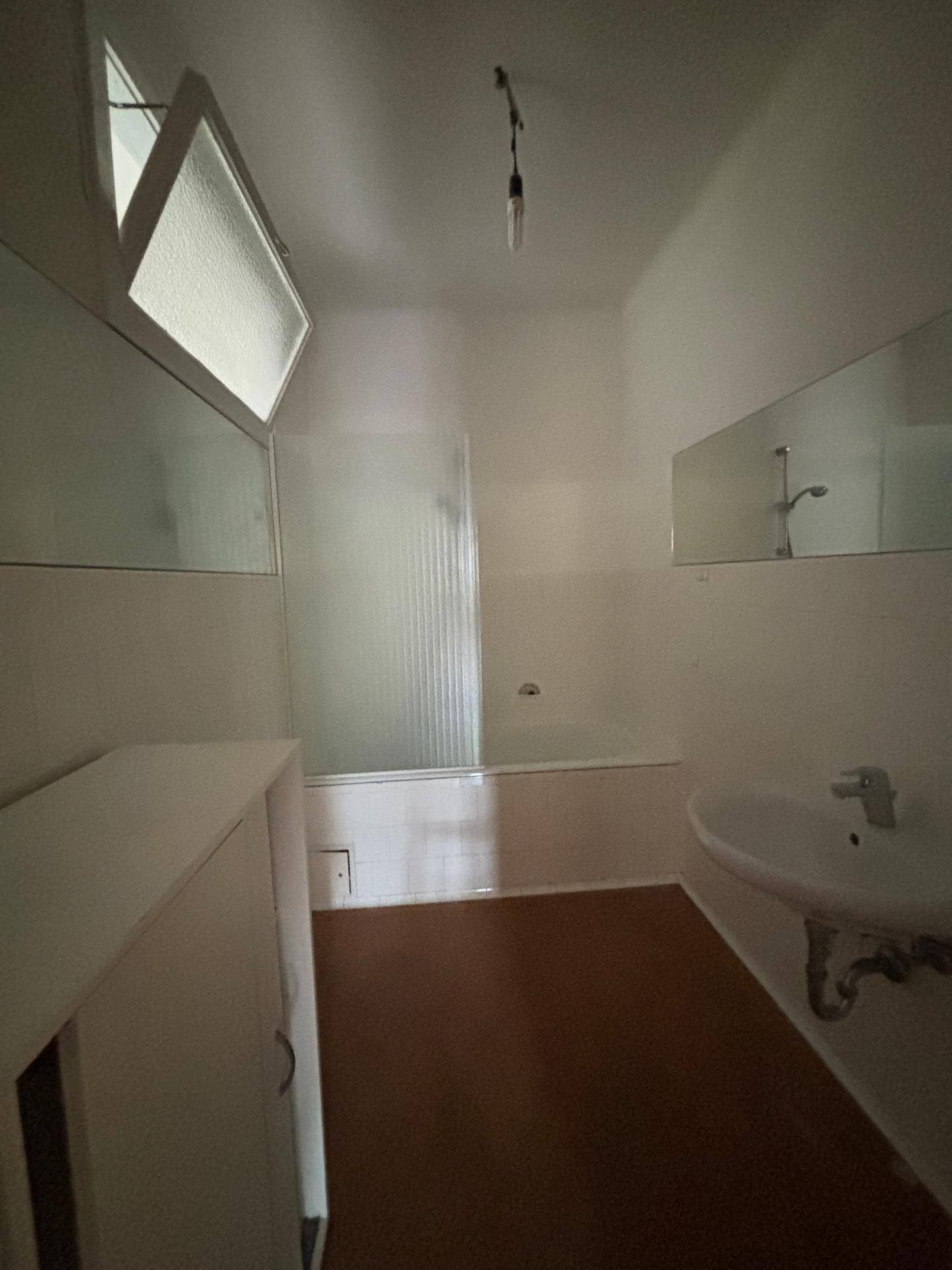 Badezimmer mit Badewanne, Waschbecken und einem kleinen Fenster für natürliche Belüftung.