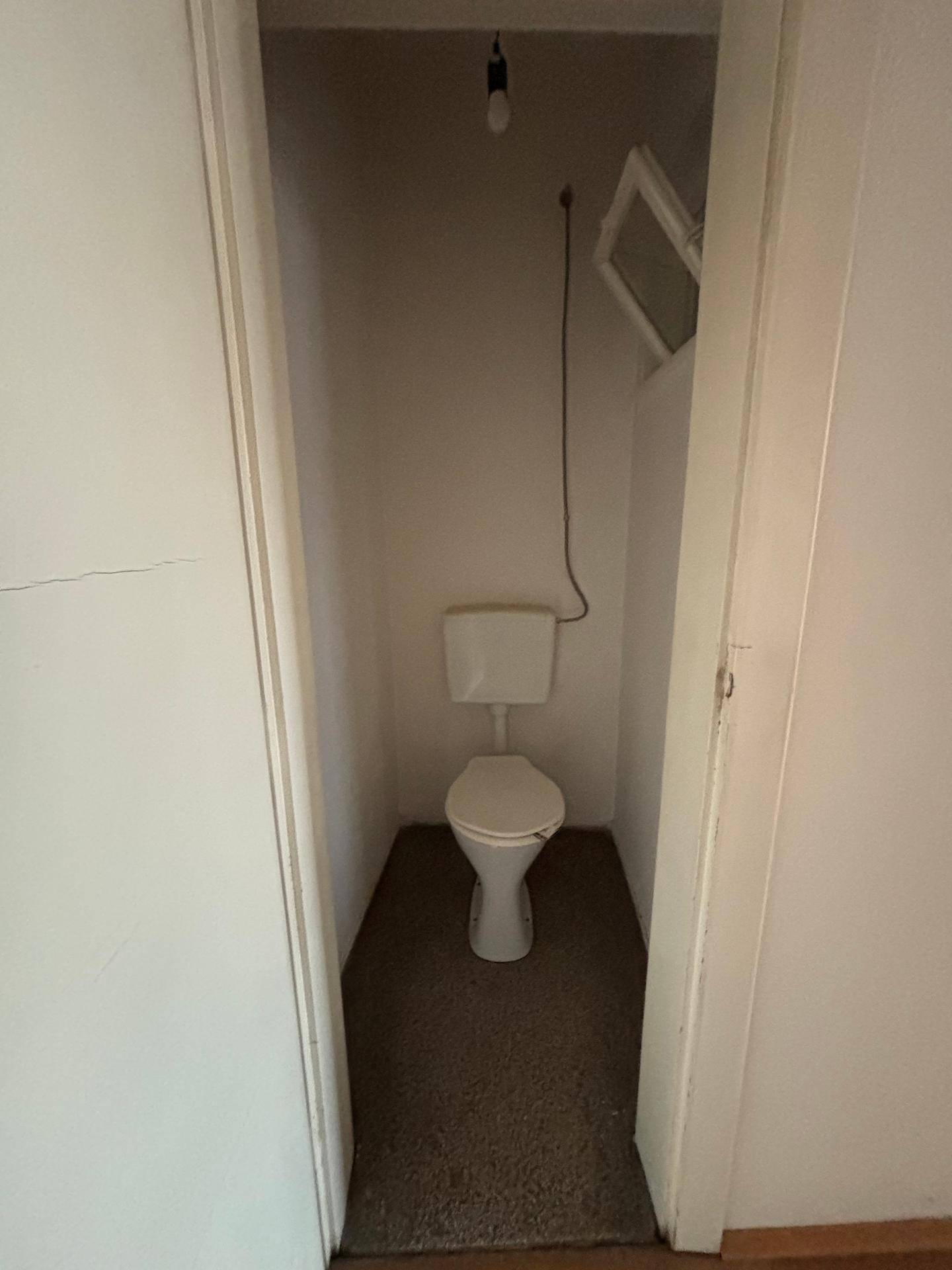 Separates WC mit Toilette und einem kleinen Fenster für Belüftung.