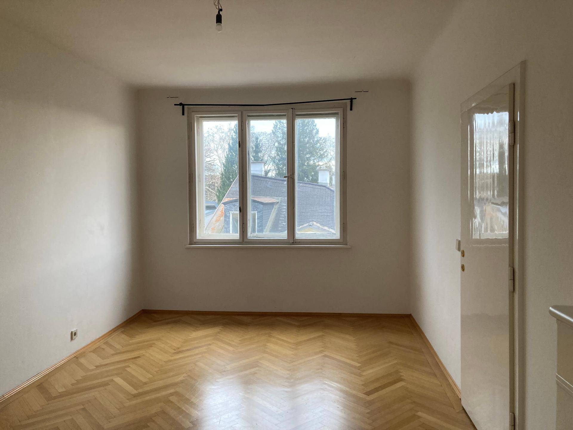 Leeres Zimmer mit klassischem Fischgrätparkett und Blick auf die umliegenden Dächer.