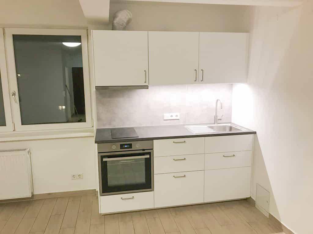 Moderne Küchenzeile mit weißen Schränken, integriertem Backofen und Spüle in hellem Raum.
