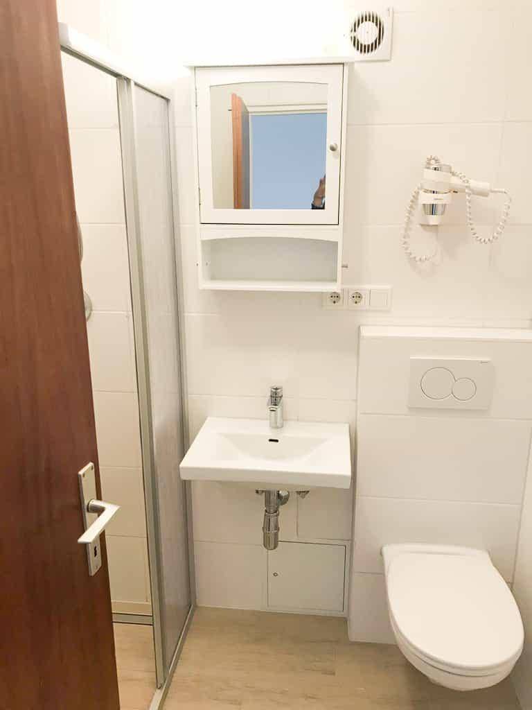 Modernes Badezimmer mit Dusche, Waschbecken, Toilette und Spiegelschrank in Weiß.