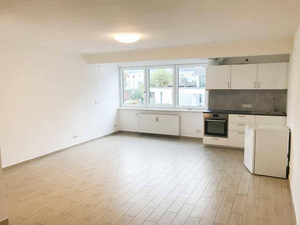 Geräumiger Wohnbereich mit integrierter Küchenzeile, großen Fenstern und hellem Laminatboden.