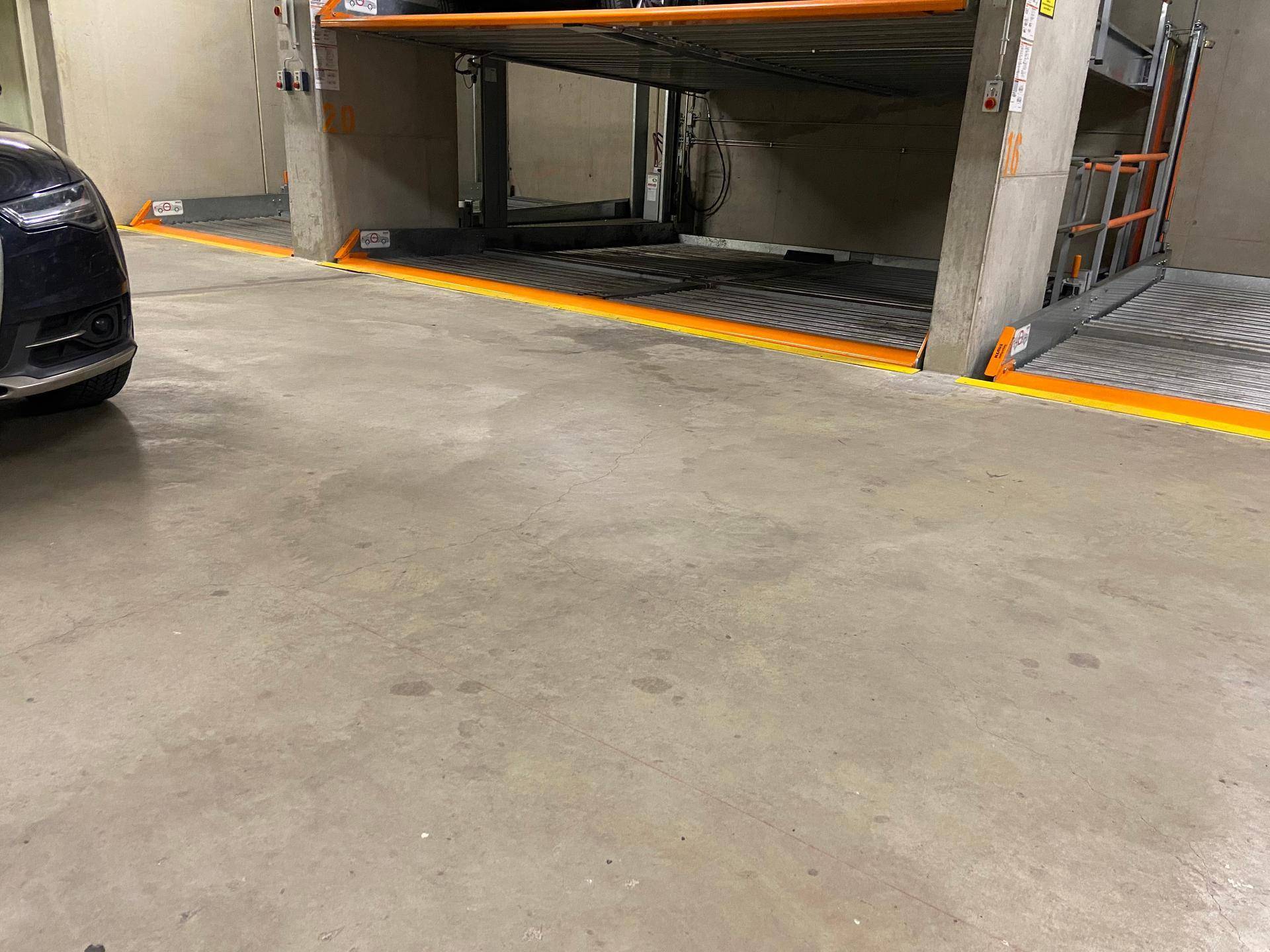 Betonboden in der Tiefgarage mit Zugang zu den Duplex-Parkplätzen und einem geparkten Auto.
