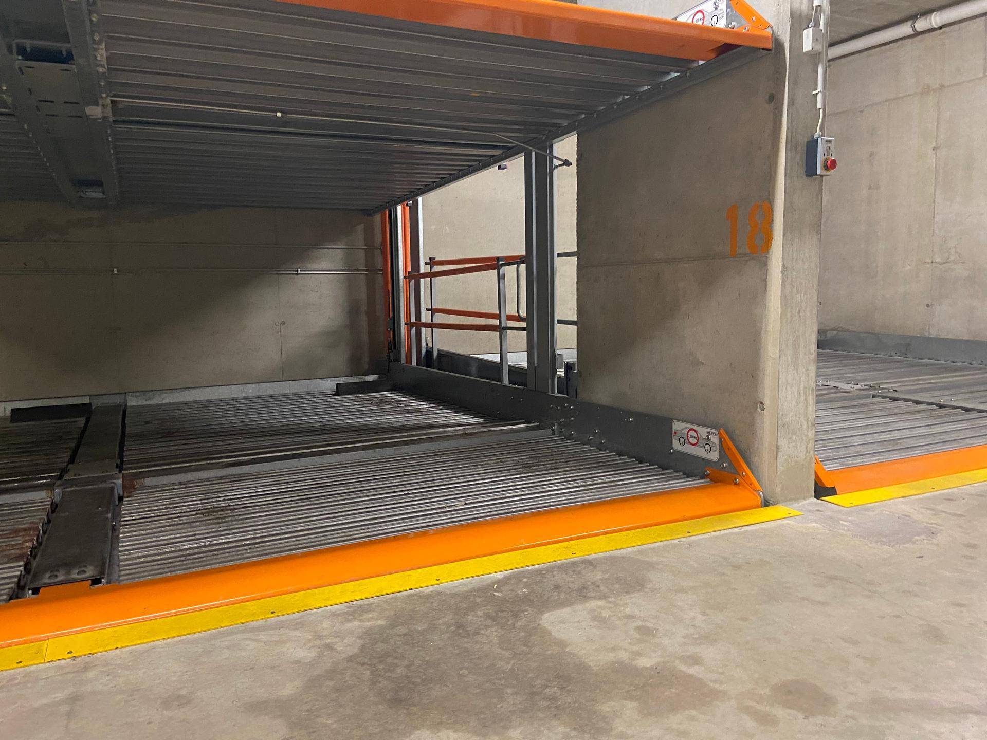 Einfahrt zu einem Duplex-Parkplatz in der Tiefgarage mit robusten Metallkonstruktionen und Betonwänden.