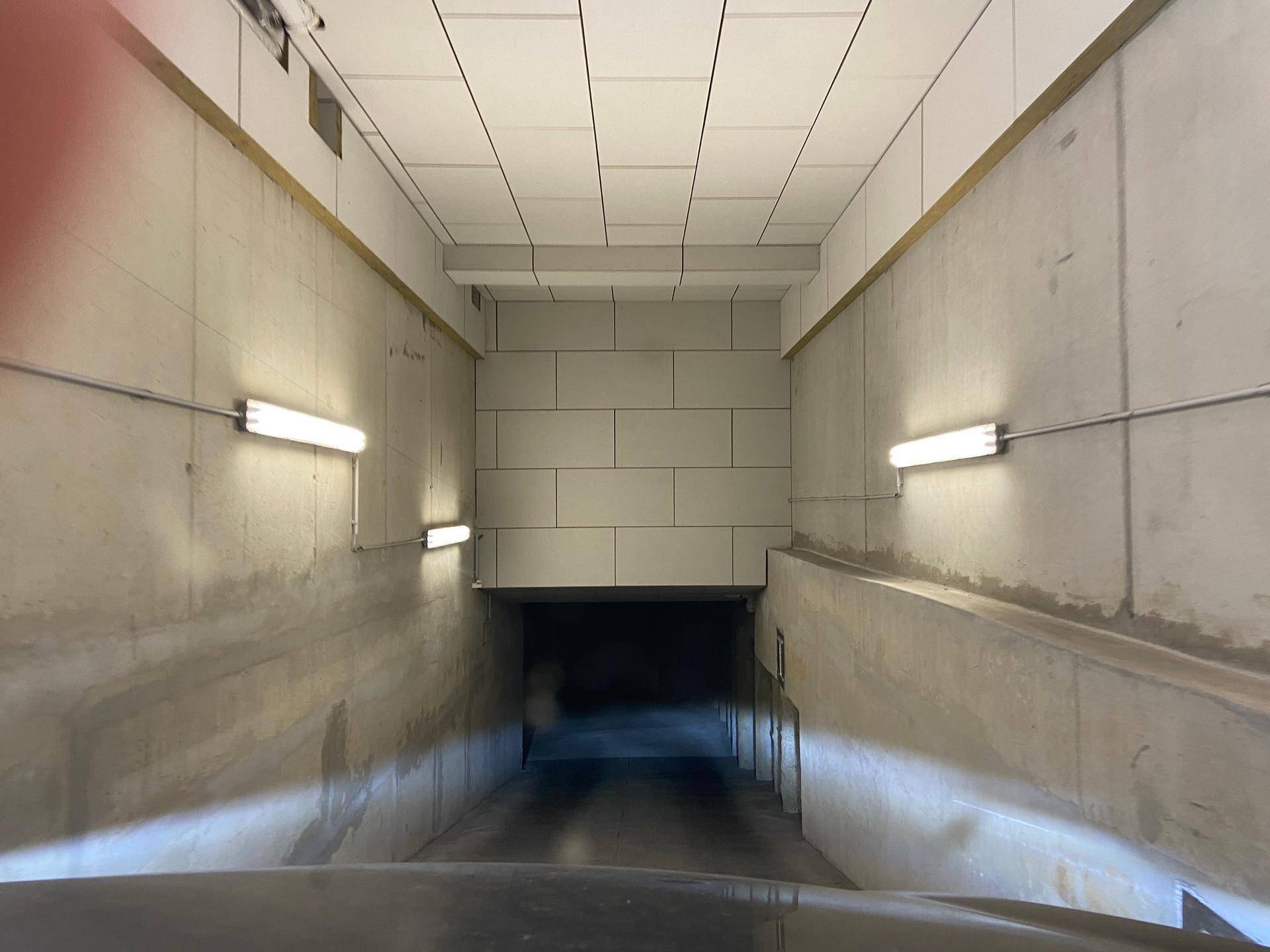 Zufahrtsrampe zur Tiefgarage mit hellen Wandleuchten und glatten Betonwänden.