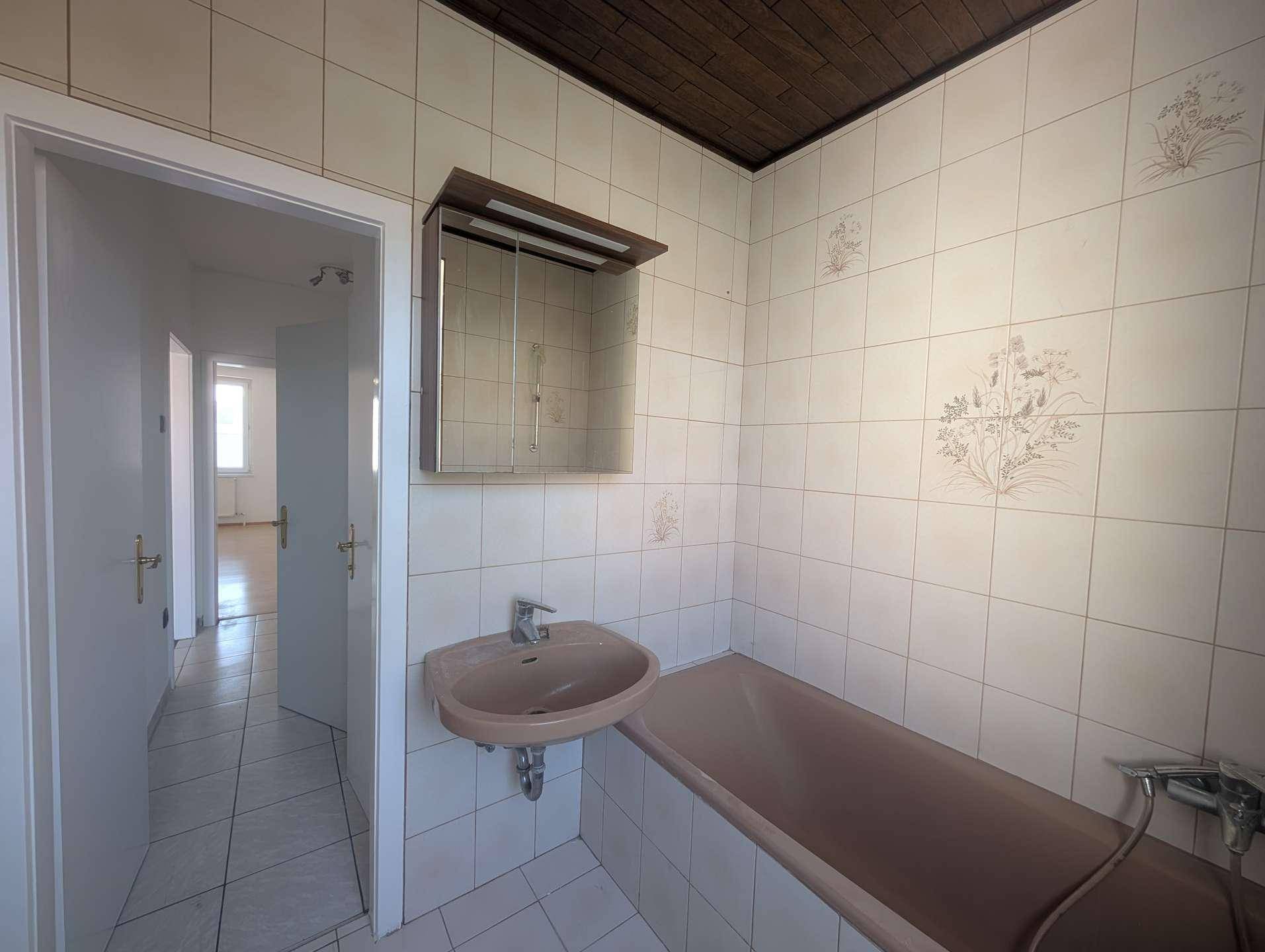 Badezimmer mit Waschbecken, Badewanne und gefliesten Wänden, die einen Blick in den Flur bieten.