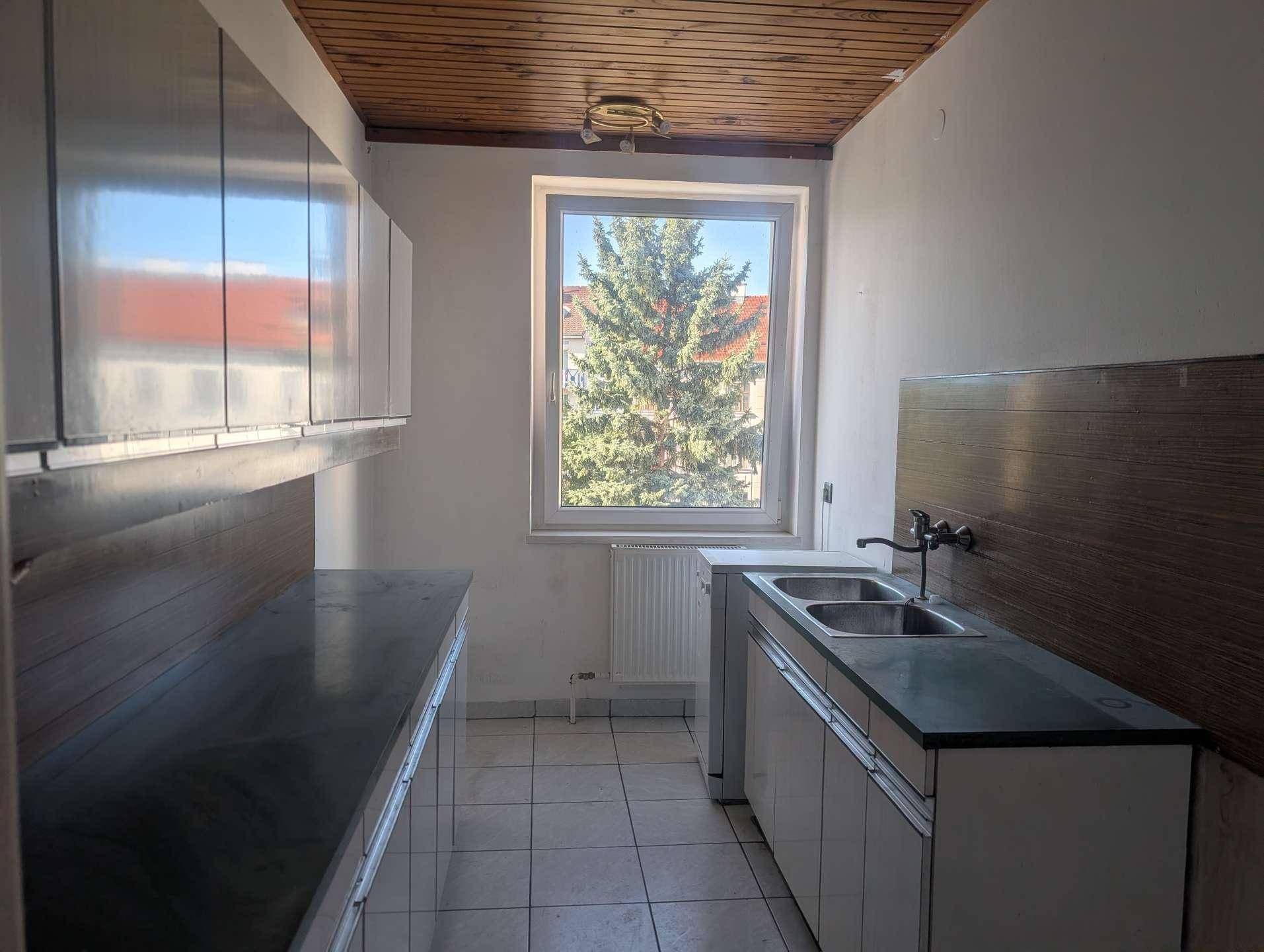 Einfache Küche mit Spüle, Arbeitsplatten und Oberschränken, mit Blick auf einen Baum.