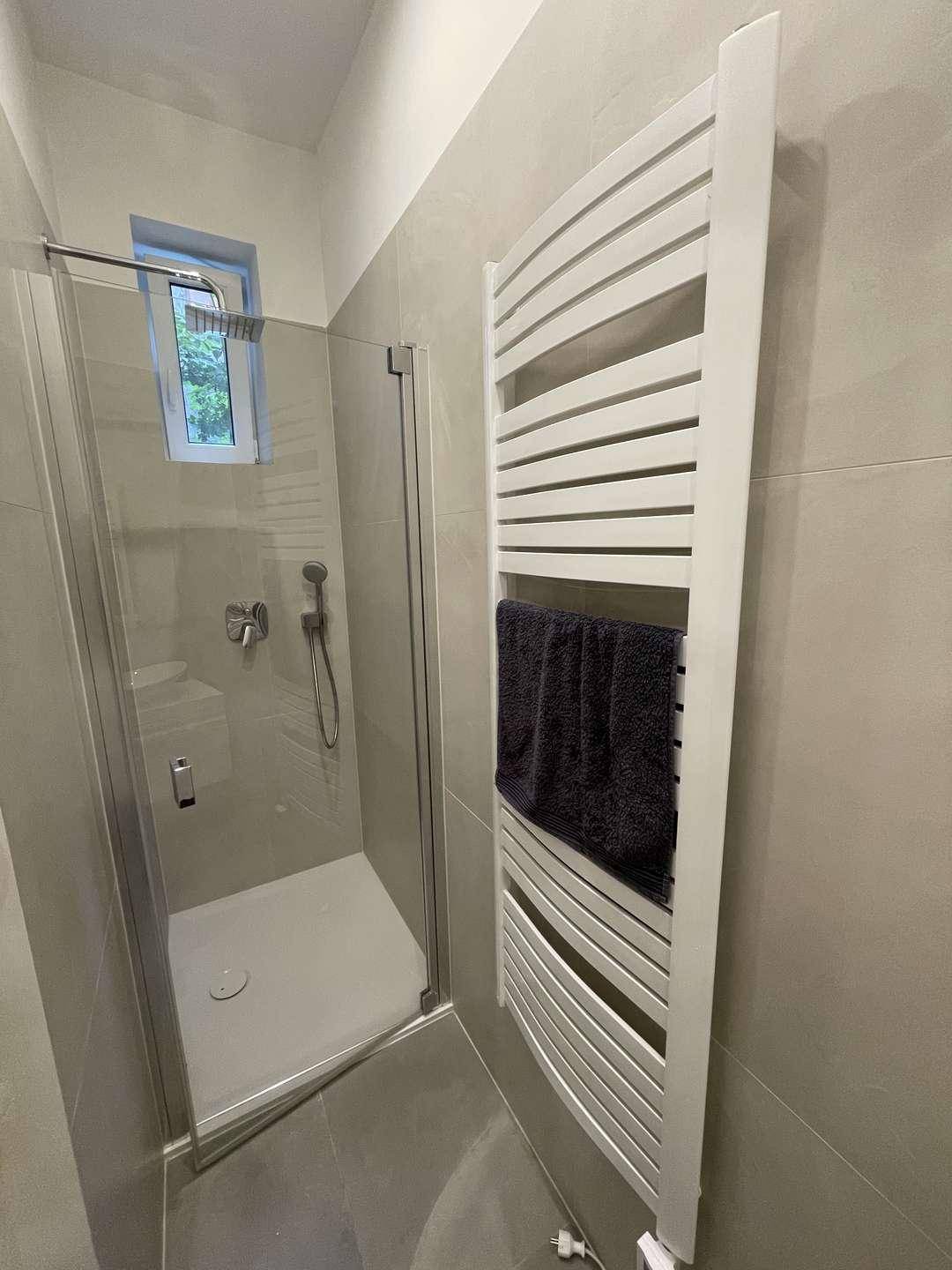Modernes Badezimmer mit ebenerdiger Dusche, beheiztem Handtuchhalter und grauen Fliesen.
