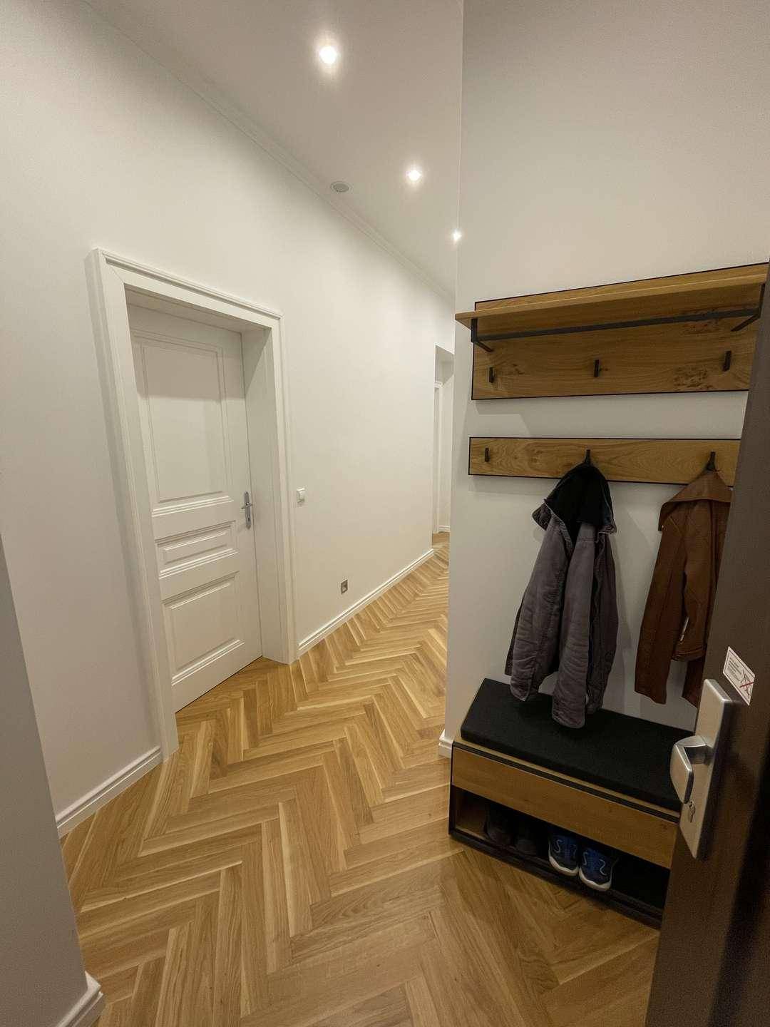 Heller Flur mit Garderobe, Sitzbank und elegantem Fischgrätparkettboden.