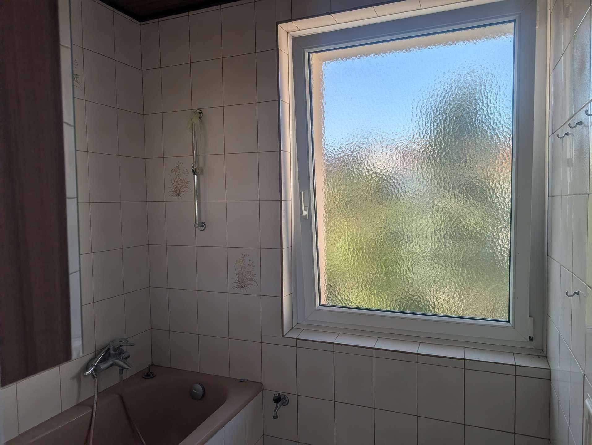 Badezimmer mit Badewanne, Fliesenwänden und einem Fenster, das für Belüftung sorgt.