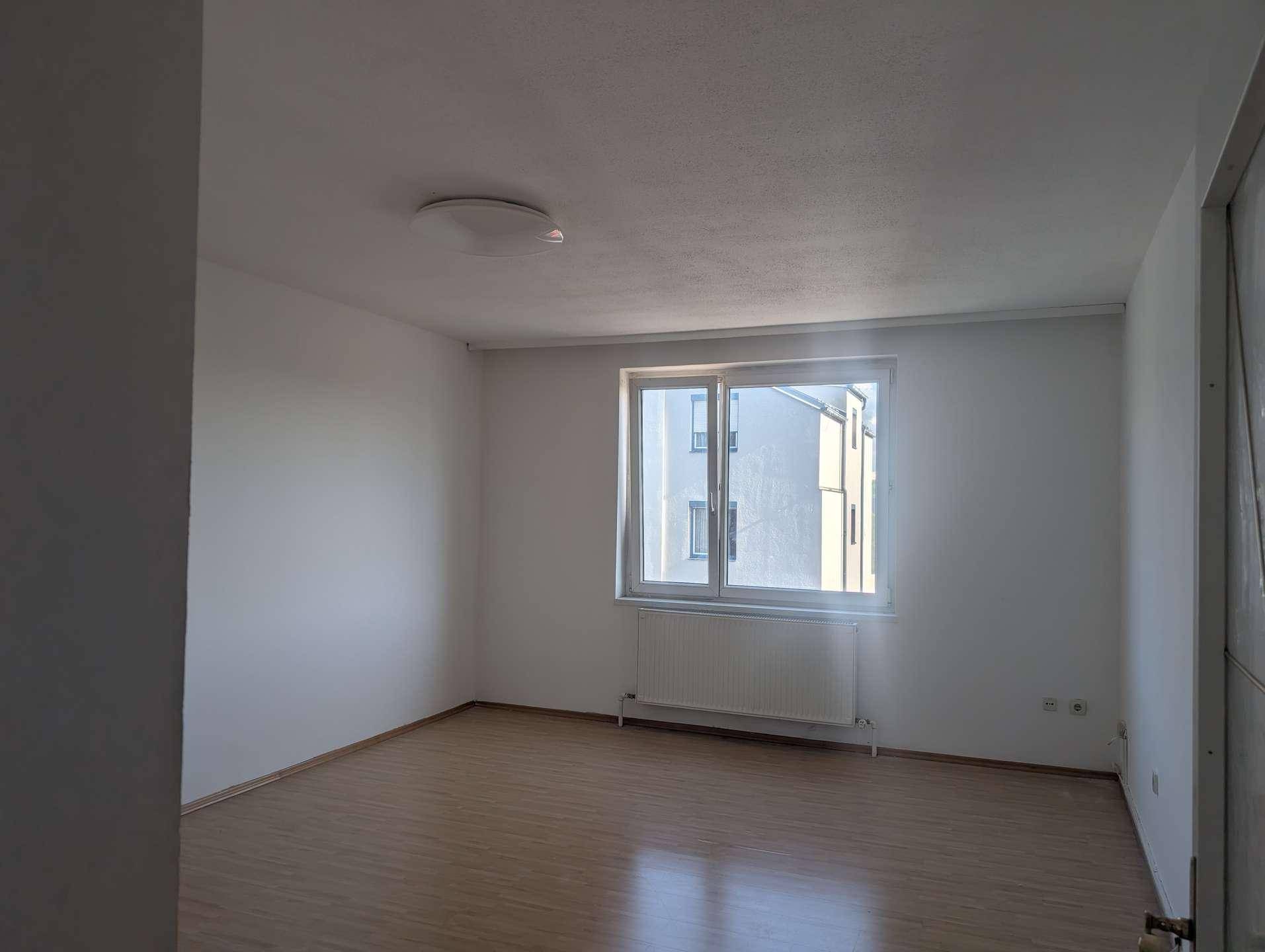 Helles, leeres Zimmer mit Laminatboden und großem Fenster, bereit zur individuellen Gestaltung.