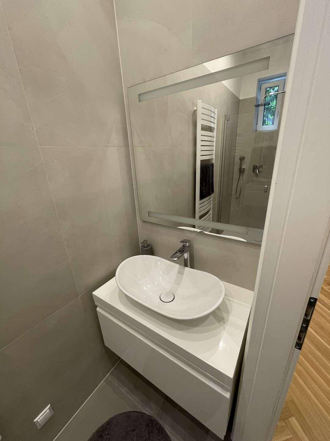 Badezimmer mit modernem Aufsatzwaschbecken, großem Spiegel und grauen Wandfliesen.