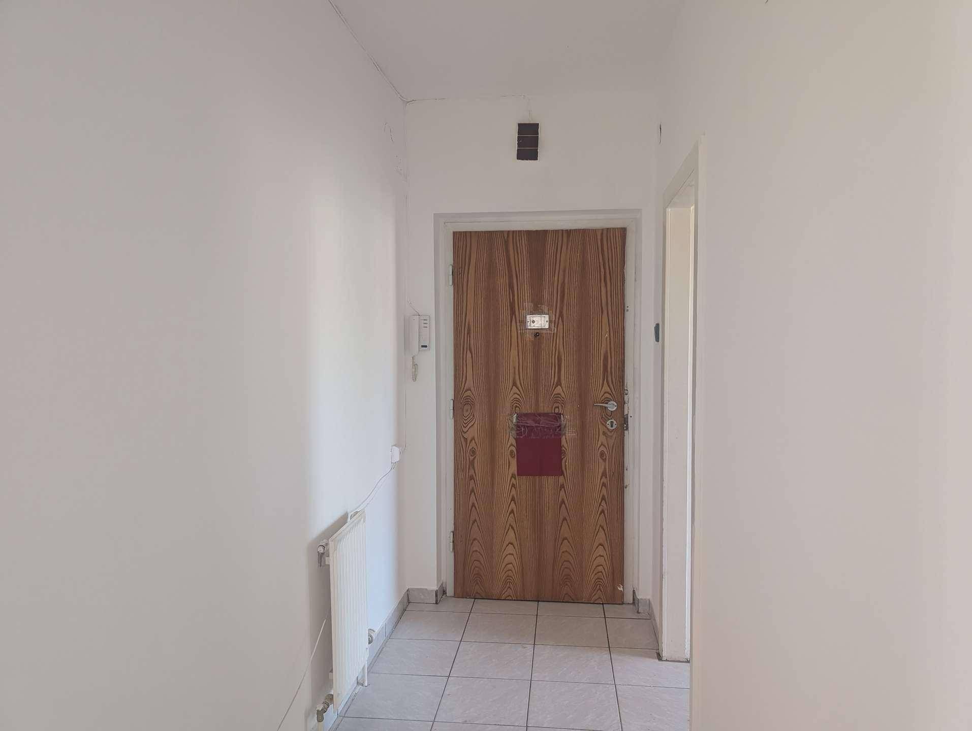 Heller Flur mit Fliesenboden und einer Holztür, die in die Wohnung führt.