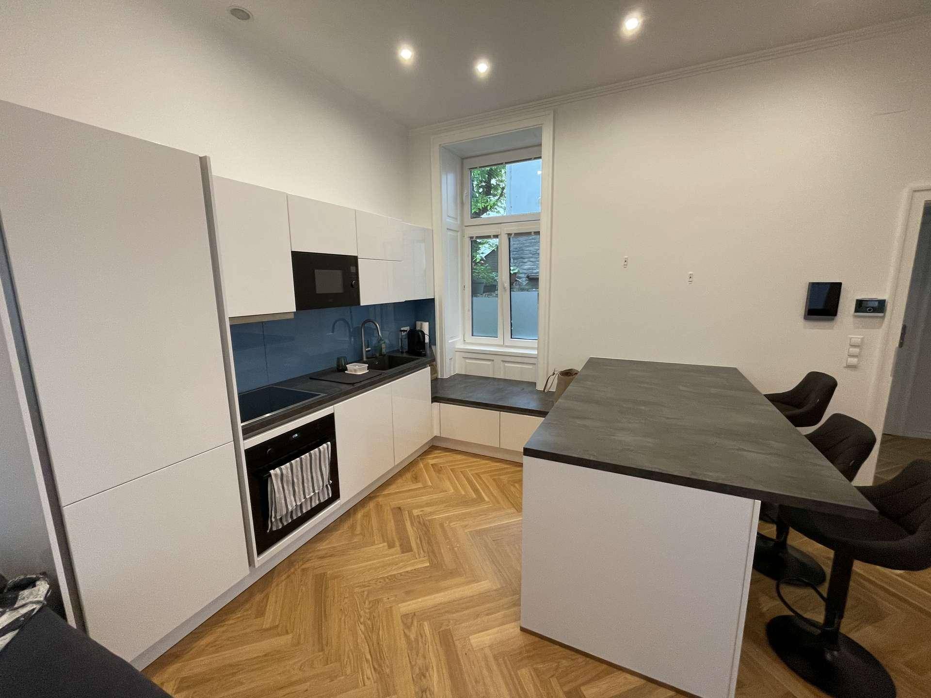 Moderne Einbauküche mit weißen Schränken, dunkler Arbeitsplatte und einem Fenster.