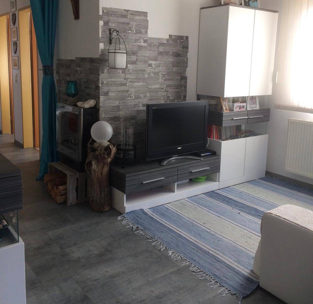 Wohnzimmer mit modernem Kamin, TV-Möbeln und einem gestreiften Teppich, gut beleuchtet durch große Fenster.