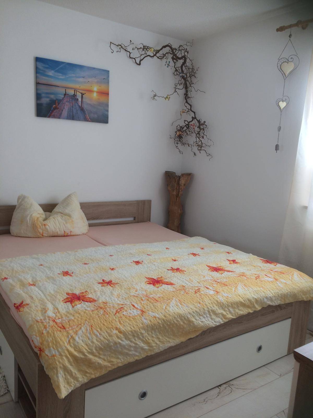 Gemütliches Schlafzimmer mit Doppelbett, hellen Wänden und dekorativen Elementen, gut beleuchtet durch ein Fenster.