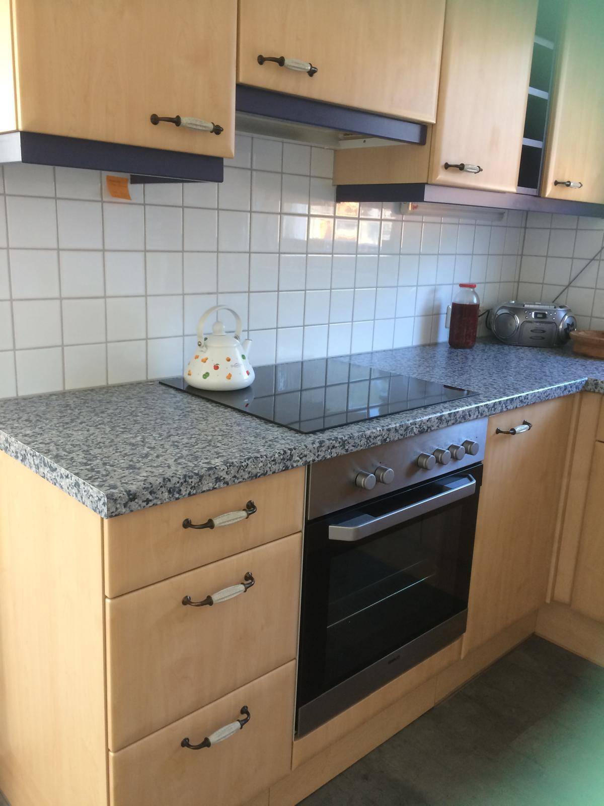 Funktionale Küche mit hellen Holzschränken, Granitarbeitsplatte und integriertem Induktionskochfeld und Backofen.