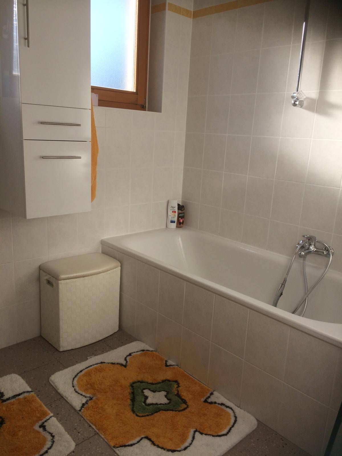 Helles Badezimmer mit Badewanne, weißen Fliesen und einem Fenster für natürliches Licht.