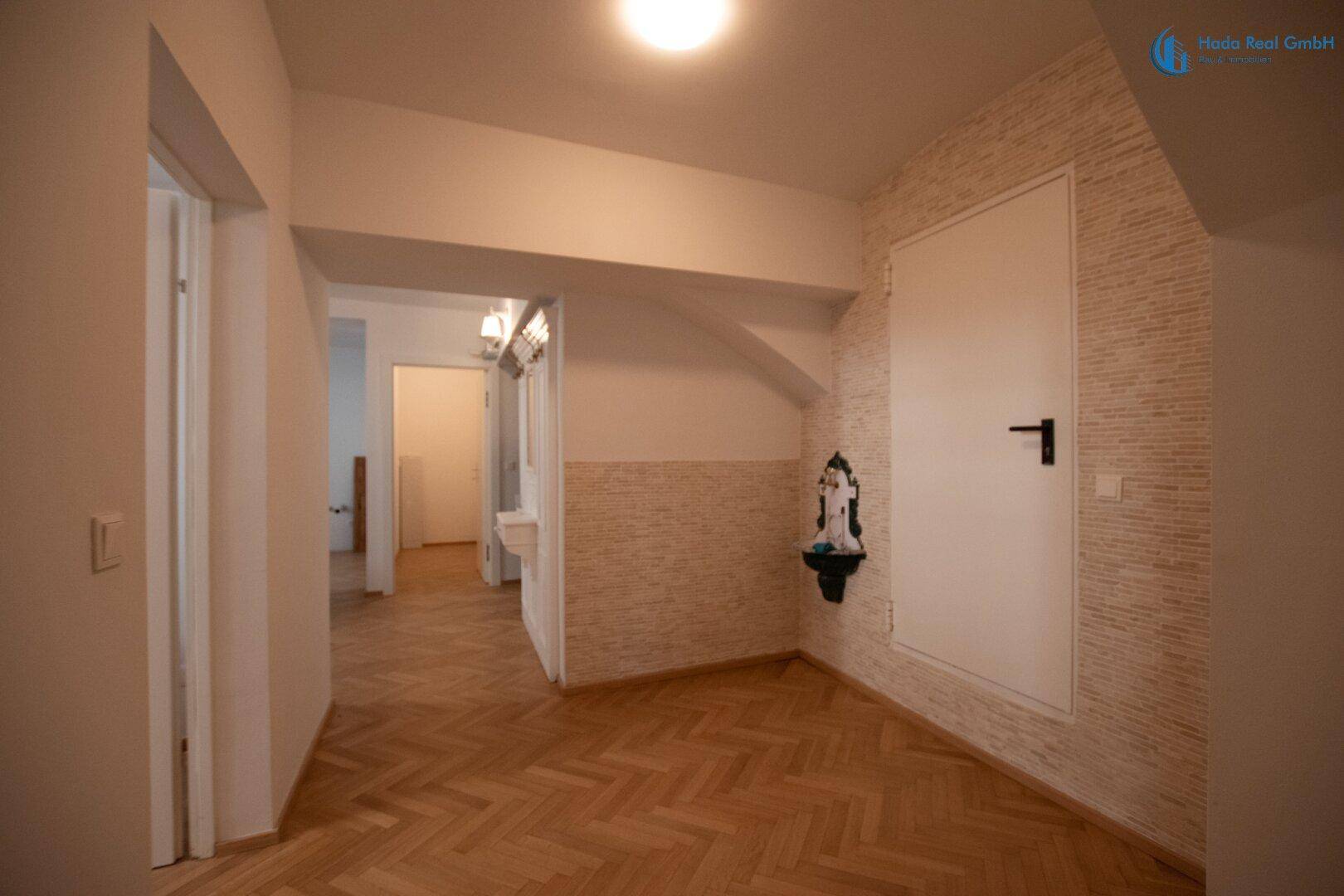 Flur mit Fischgrätparkett und dekorativer Wandverkleidung, der zu verschiedenen Räumen führt.