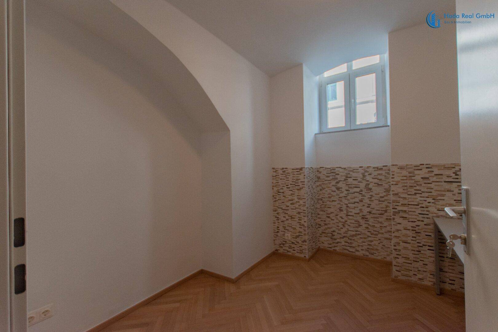 Kleiner Raum mit Fischgrätparkett, Fenster und dekorativer Wandverkleidung, bietet vielseitige Nutzung.