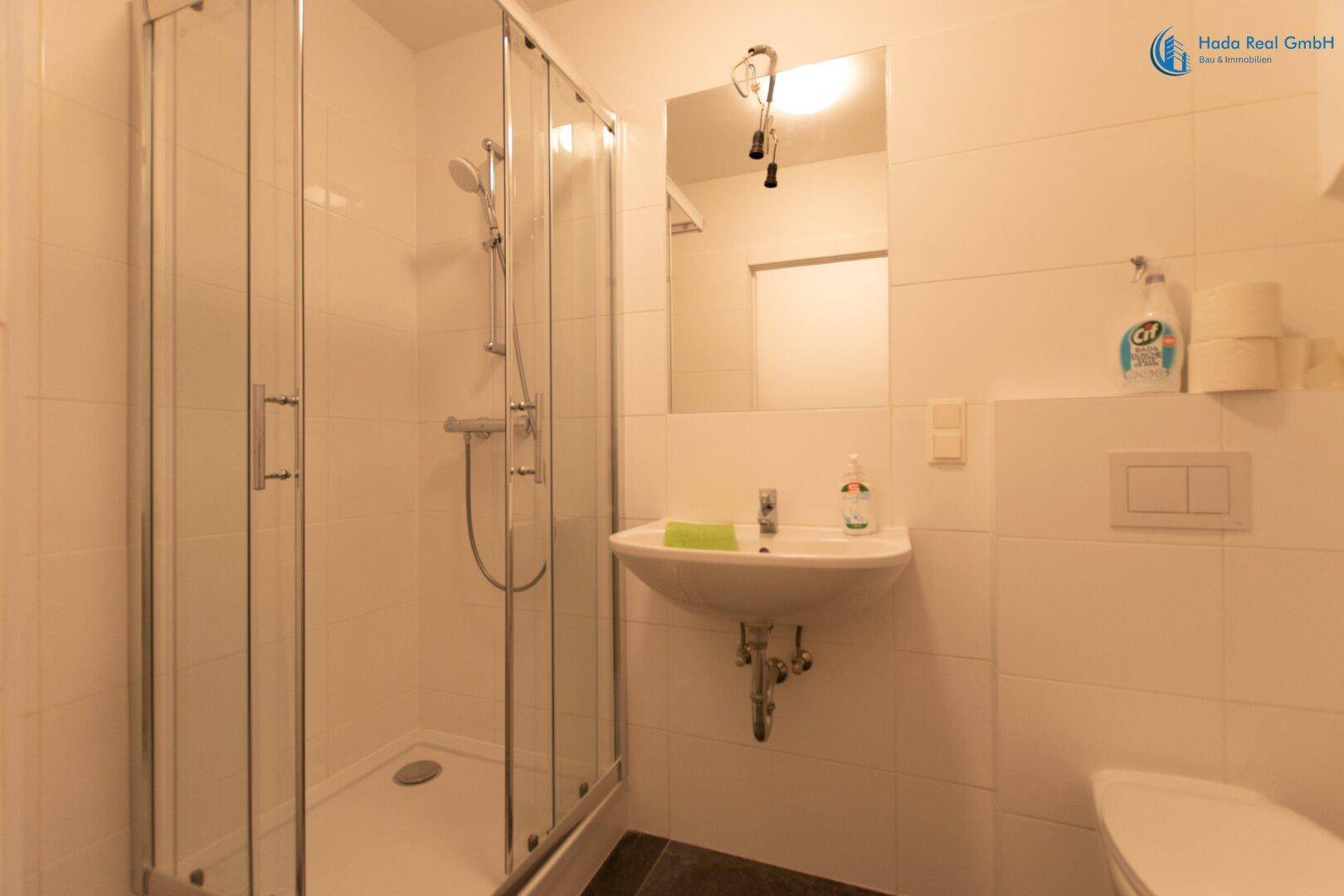 Modernes Badezimmer mit Duschkabine, Waschbecken und Toilette, komplett gefliest in Weiß.