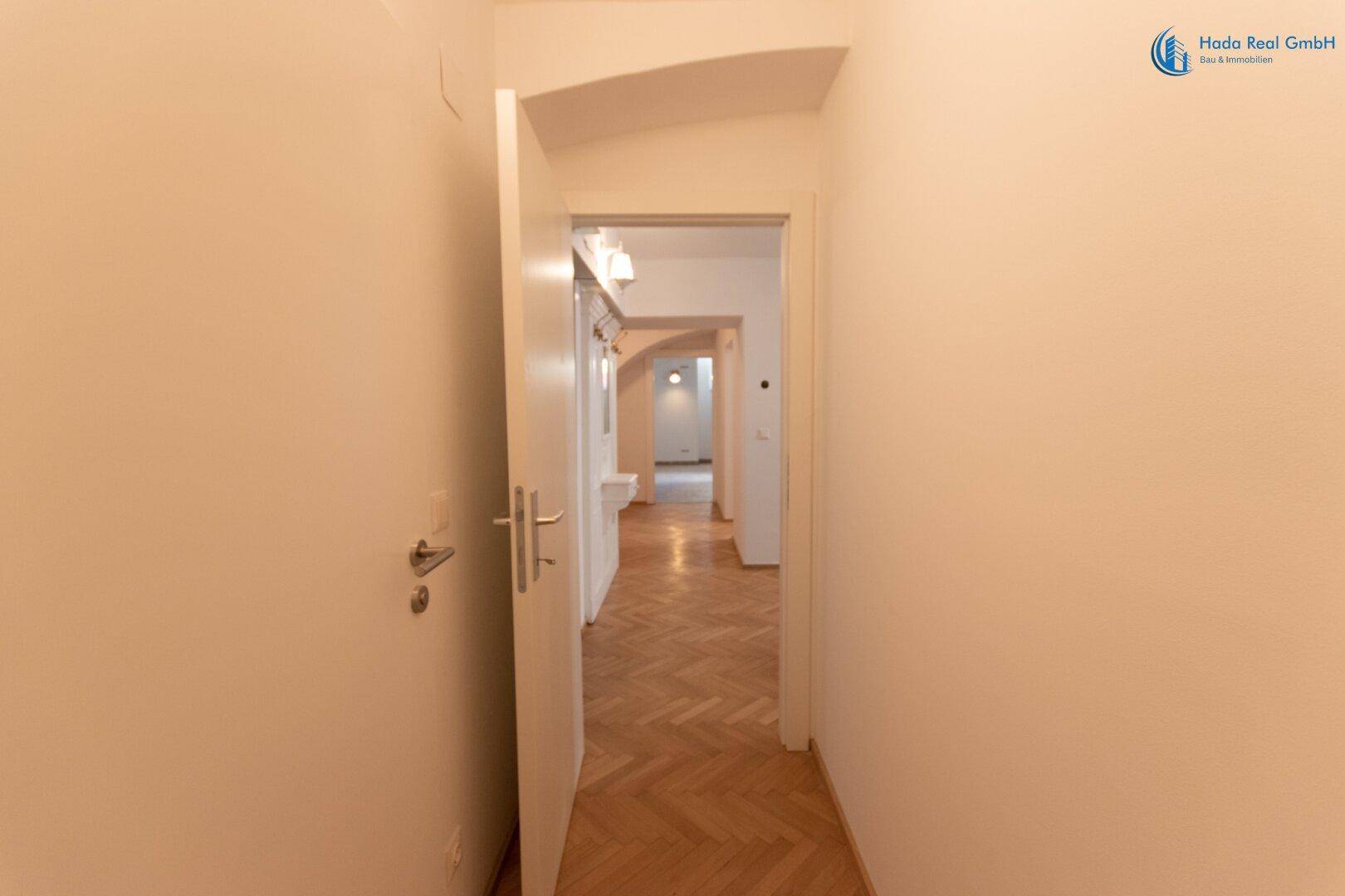 Langer Flur mit elegantem Fischgrätparkett, der einen Durchgang zu weiteren Wohnbereichen ermöglicht.