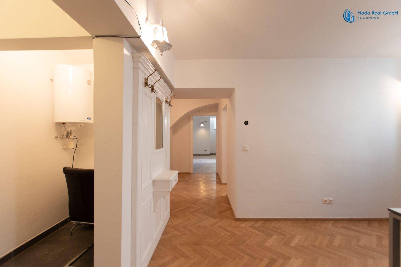 Eingangsbereich mit Fischgrätparkett und Garderobe, daneben ein Heizkessel in einer Nische.