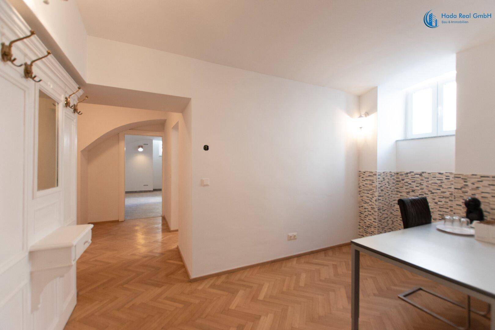 Heller Flur mit Fischgrätparkett, einem Tisch und einem Fenster, das natürliches Licht hereinlässt.