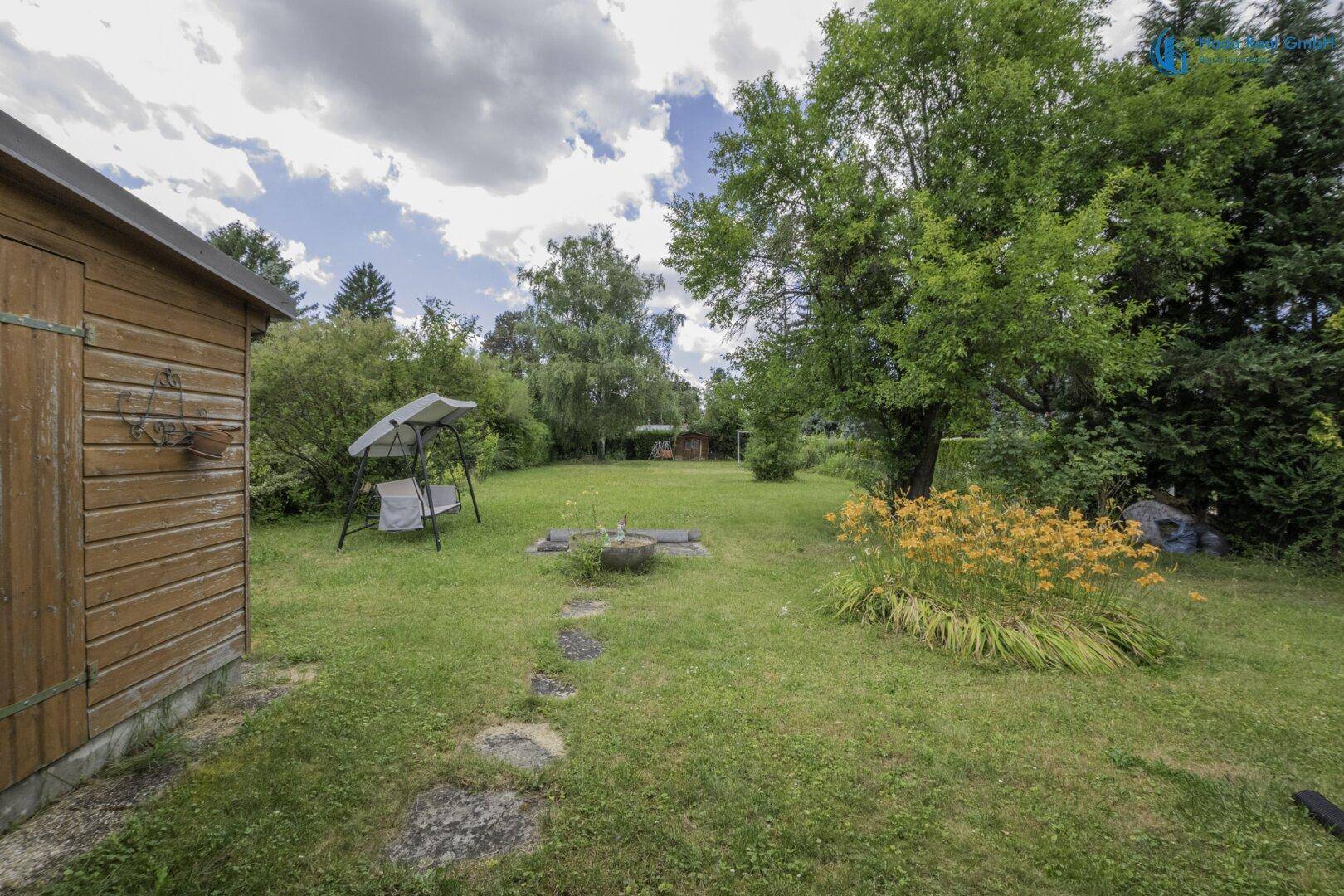 Grüner Gartenbereich mit Schaukel und einem kleinen Holzschuppen, umgeben von Bäumen.