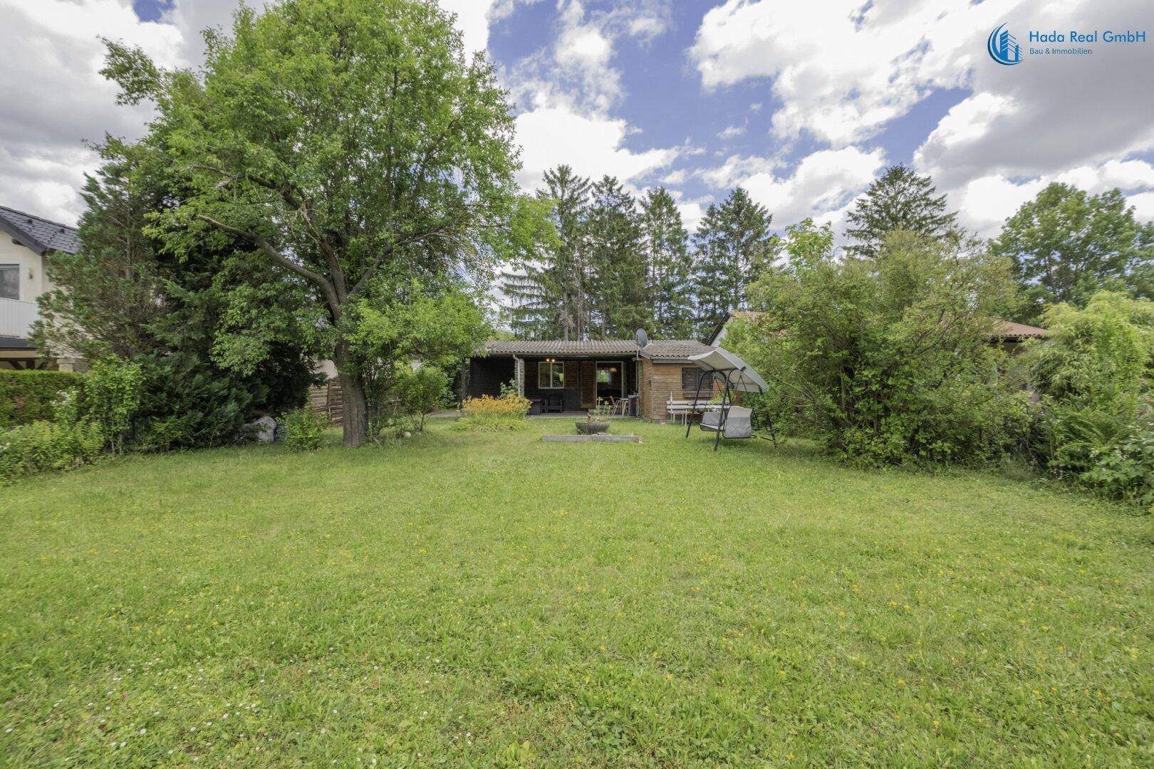 Weitläufiger Gartenbereich mit Rasenfläche und dem kleinen Holzhaus im Hintergrund.