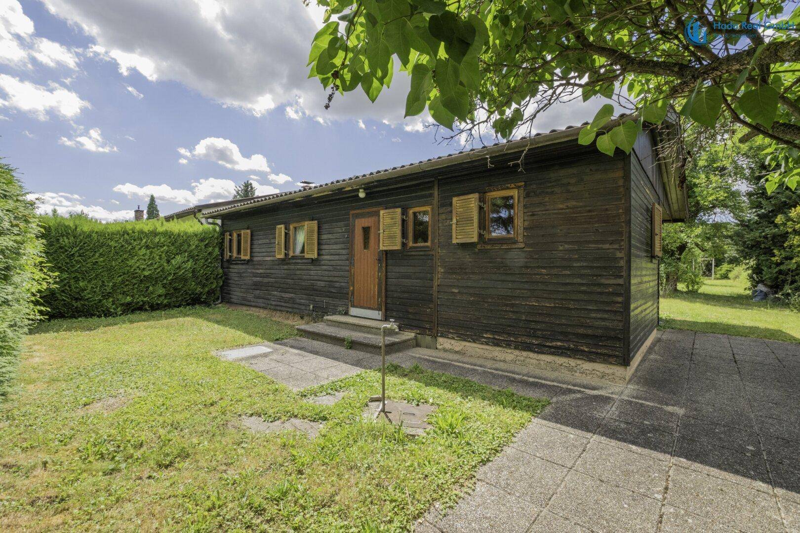 Vorderansicht des Holzhauses mit Holzfassade und gepflastertem Zugangsbereich im Grünen.