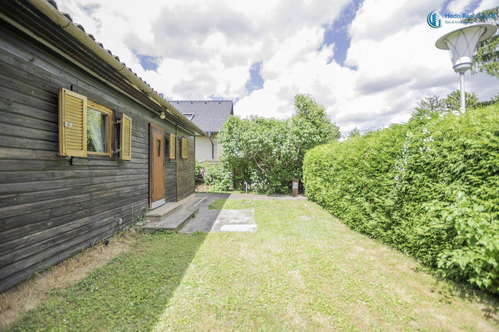 Seitenansicht des Holzhauses mit Holzfassade, Gartenweg und hoher Hecke.