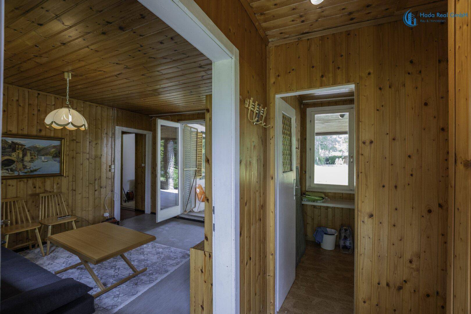 Rustikales Wohnzimmer mit Holzvertäfelung, Sofa und direktem Zugang zur Terrasse.