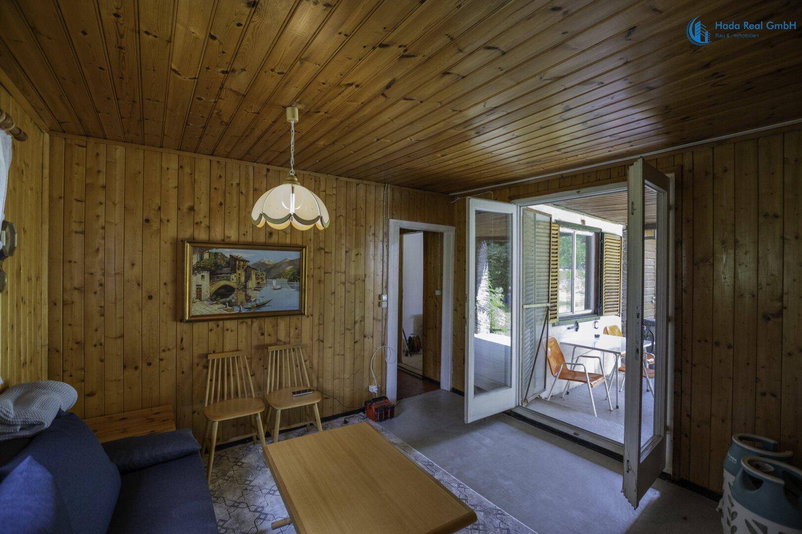 Helles Wohnzimmer mit Holzvertäfelung, traditioneller Einrichtung und Terrassenzugang durch Flügeltüren.