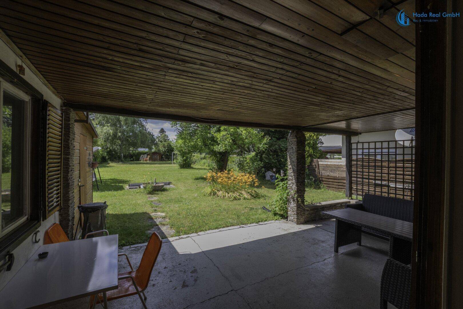 Überdachte Terrasse mit Sitzgelegenheiten und weitem Blick auf den grünen Garten.