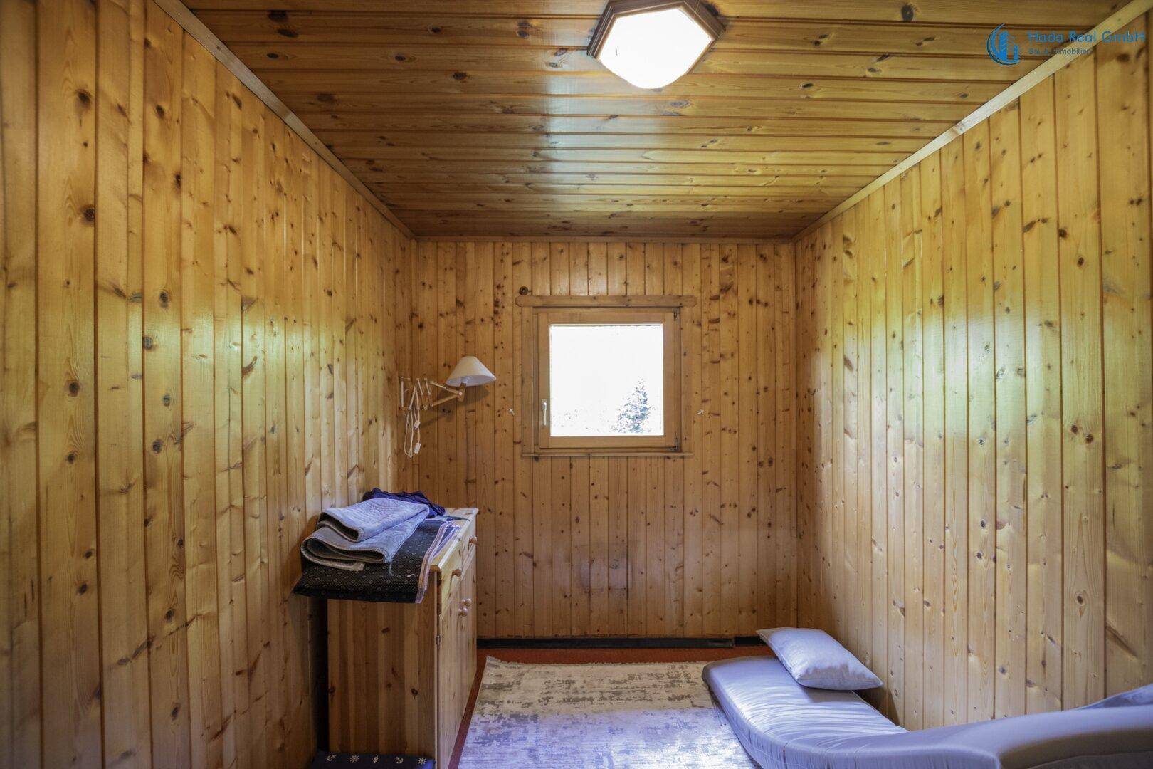 Kleines Schlafzimmer mit Holzvertäfelung, Fenster und einfacher Einrichtung, bietet Ruhe.