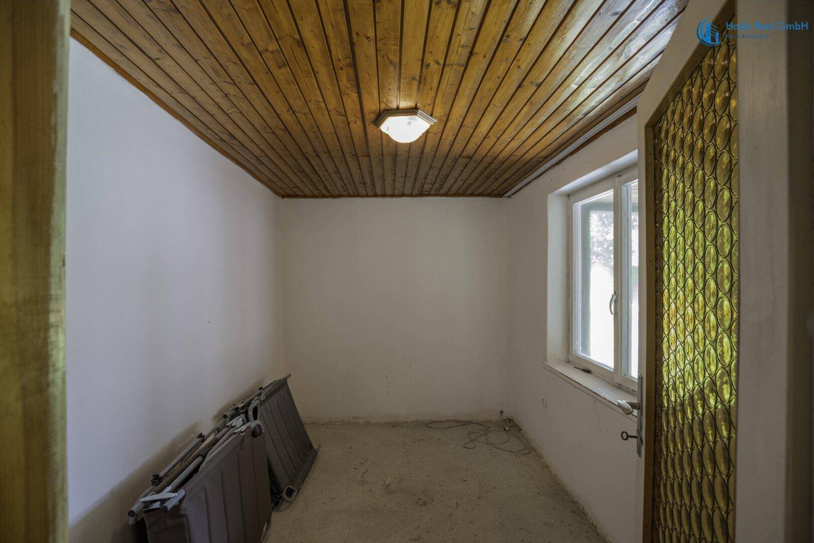 Leerer Raum mit weißen Wänden, Holzdecke und Fenster, ideal als Abstellraum nutzbar.