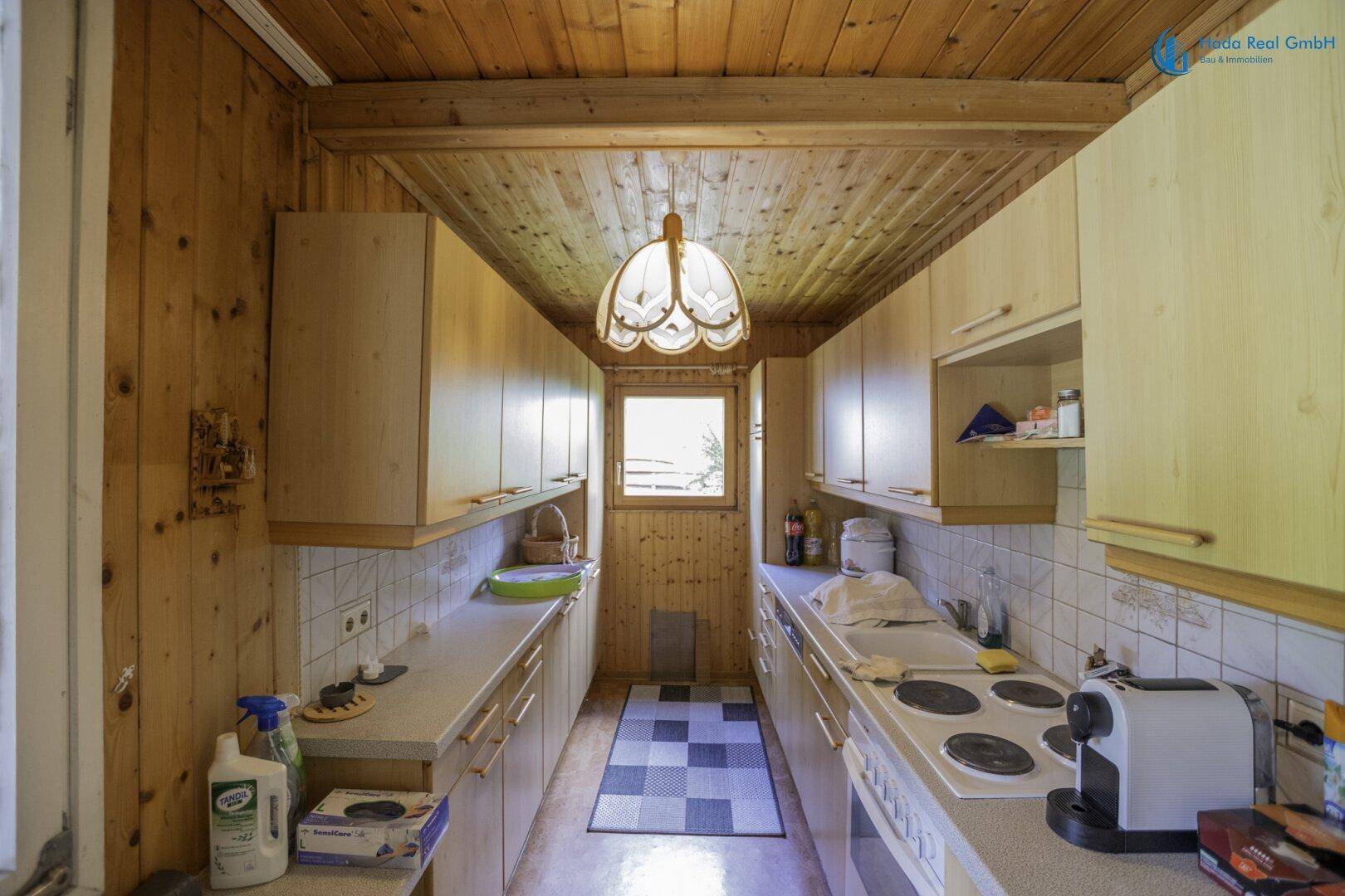 Schmale Küche mit Holzvertäfelung, Einbauschränken und Fenster, funktional eingerichtet.