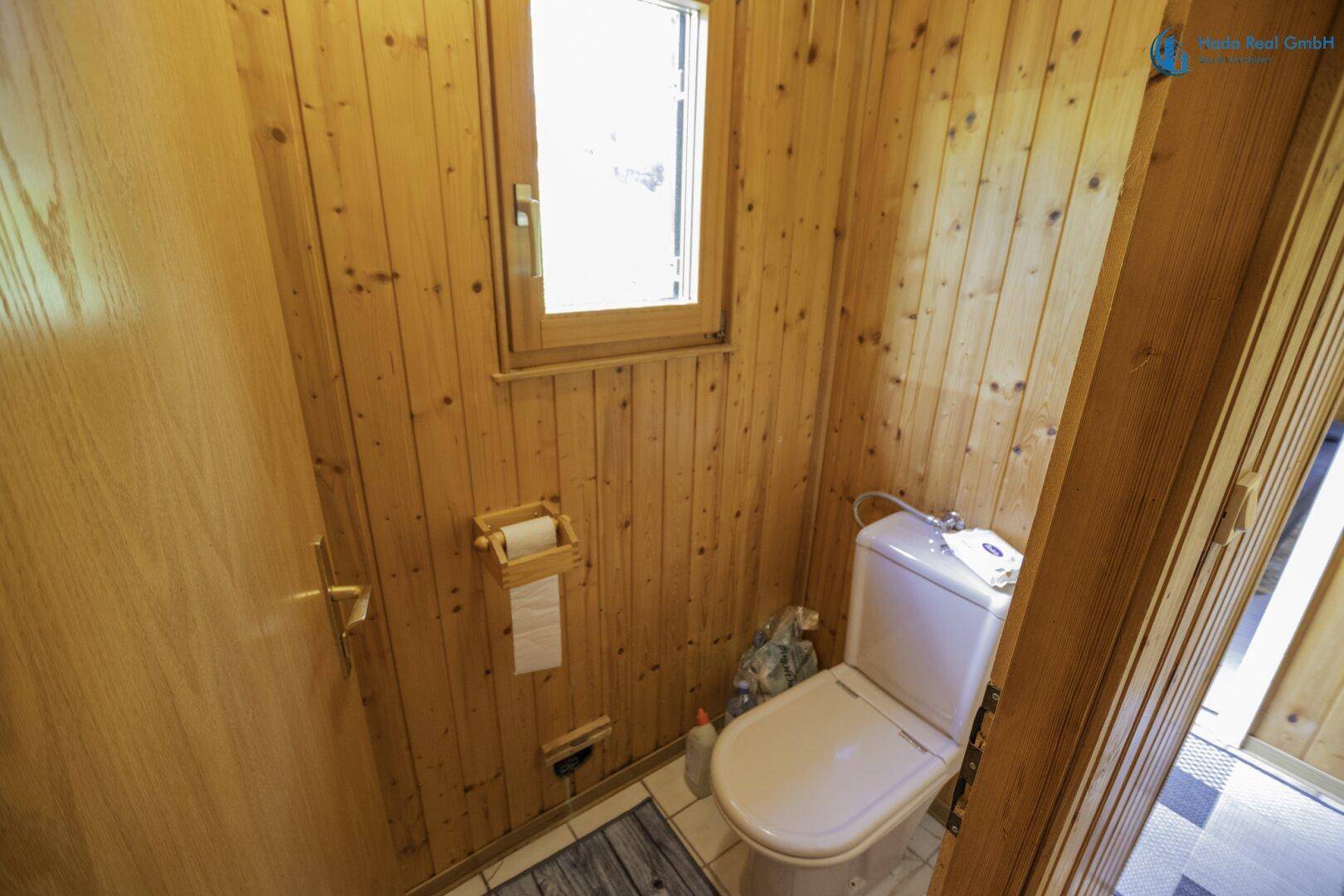 Separates WC mit Holzvertäfelung und kleinem Fenster, praktisch und einfach gehalten.