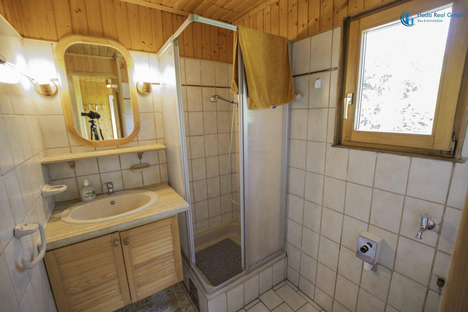 Badezimmer mit Duschkabine, Waschbecken und Fliesen im traditionellen Stil der 80er Jahre.