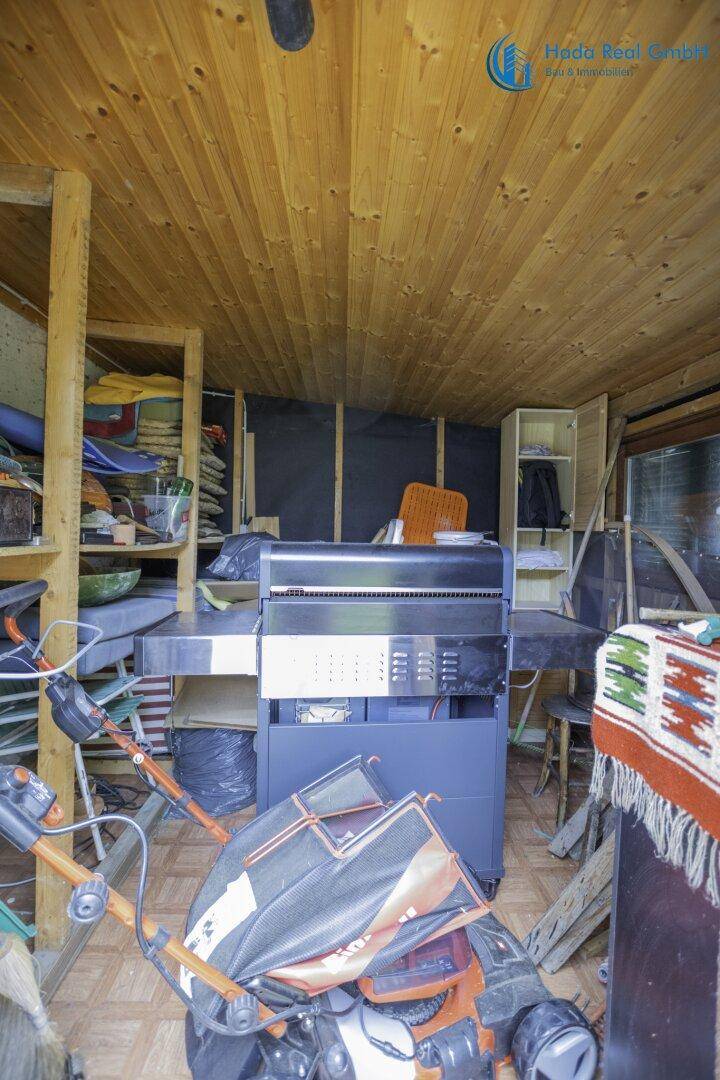 Innenansicht des Holzschuppens mit Grill, Regalen und Gartengeräten, gut organisiert.