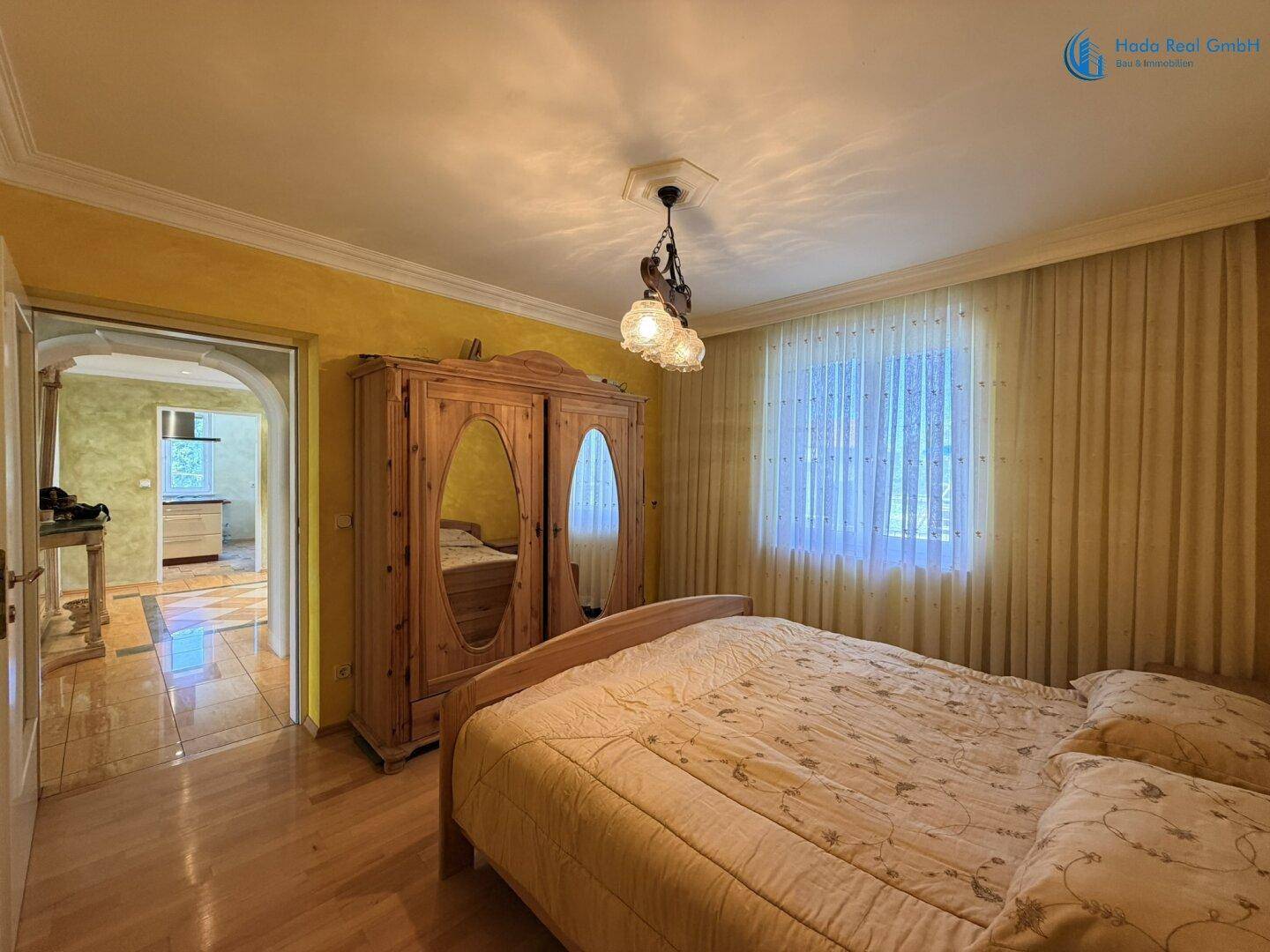 Gemütliches Schlafzimmer mit Holzbett, großem Kleiderschrank und hellem Holzboden, durch eine Tür verbunden.