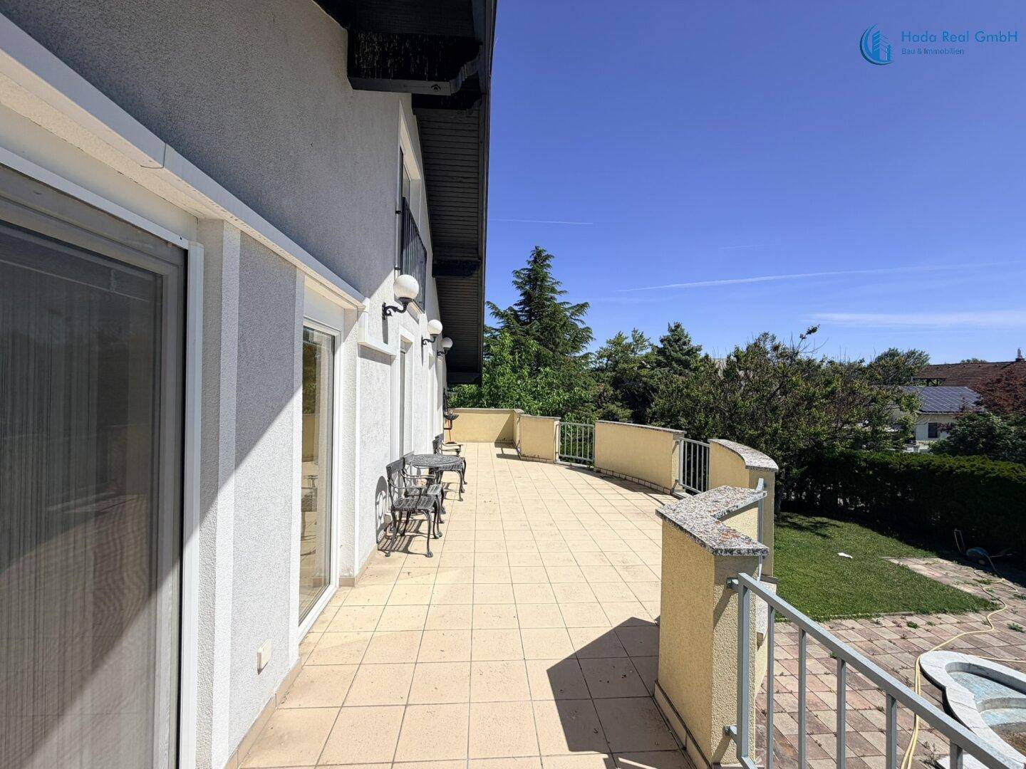 Seitenansicht des Hauses mit der großen gefliesten Terrasse und Blick ins Grüne.