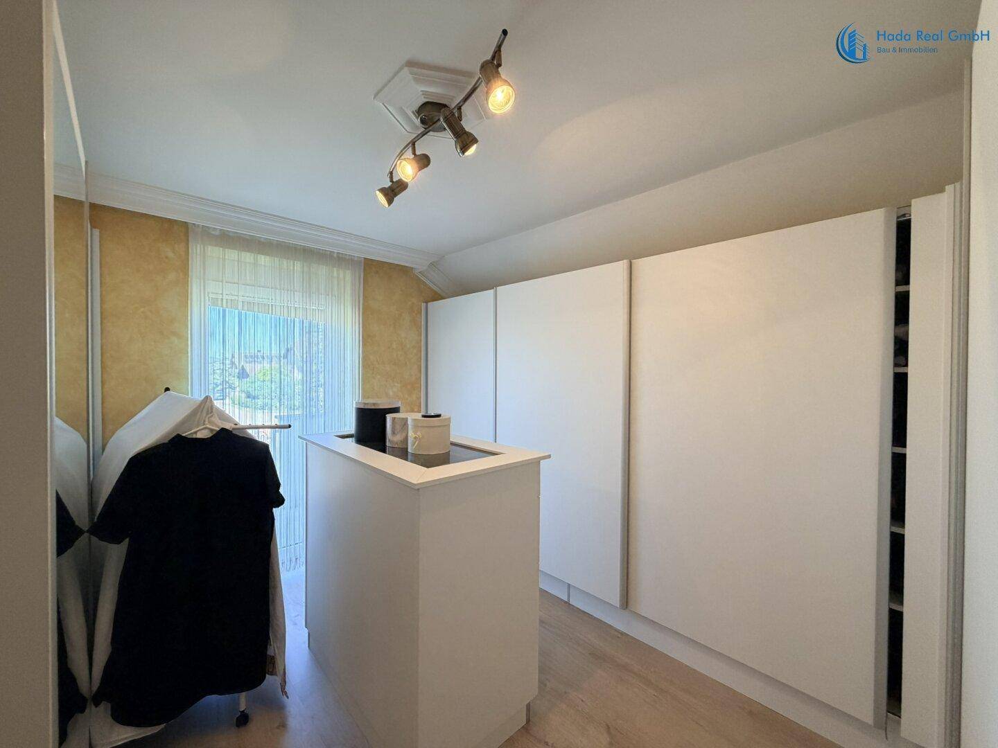 Heller Ankleidebereich mit weißen Einbauschränken und einer zentralen Insel für zusätzlichen Stauraum.