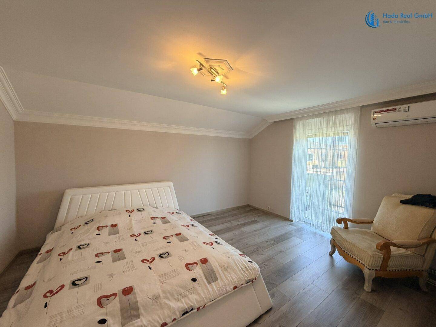 Helles Schlafzimmer mit Bett, Sessel und Klimaanlage, ausgestattet mit modernem Holzboden.