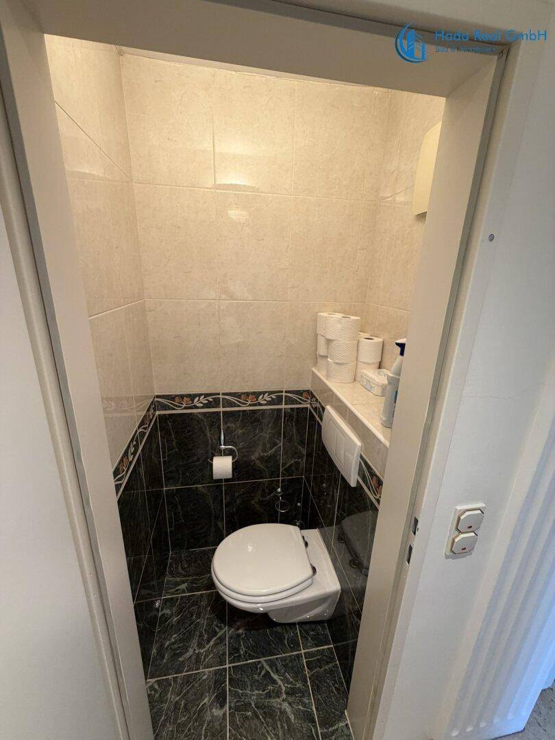 Kleines Gäste-WC mit wandhängender Toilette und dunklen, gemusterten Fliesen an den Wänden.