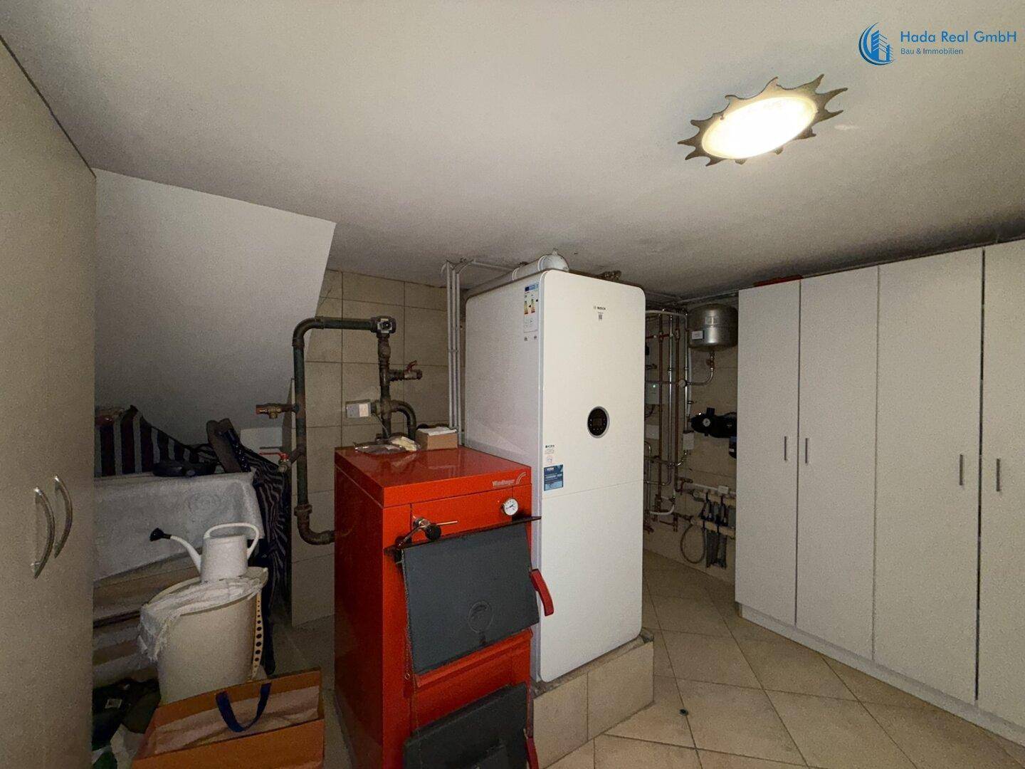 Heizungsraum mit rotem Heizkessel, weißem Lagerschrank und Dachschräge, gut organisiert.