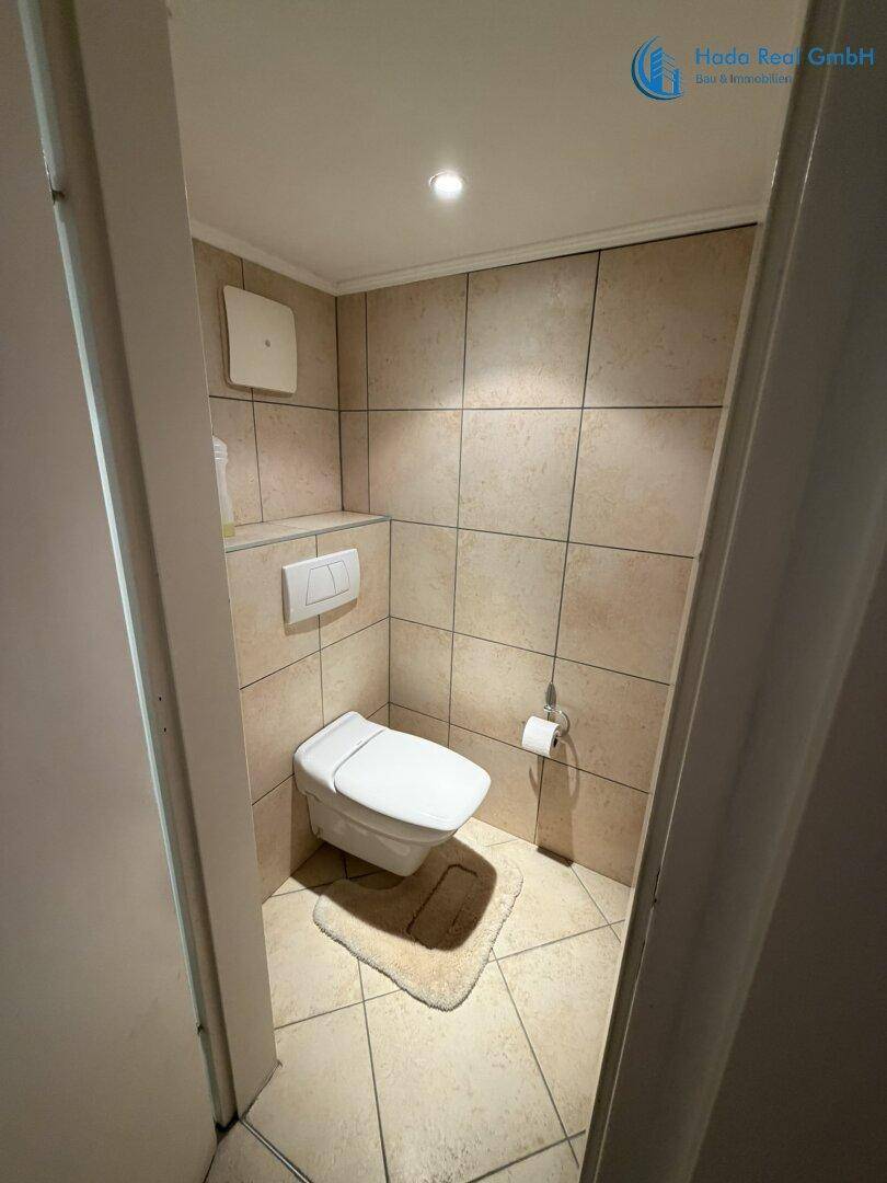 Kleines Gäste-WC mit beigefarbenen Fliesen und wandhängendem WC.