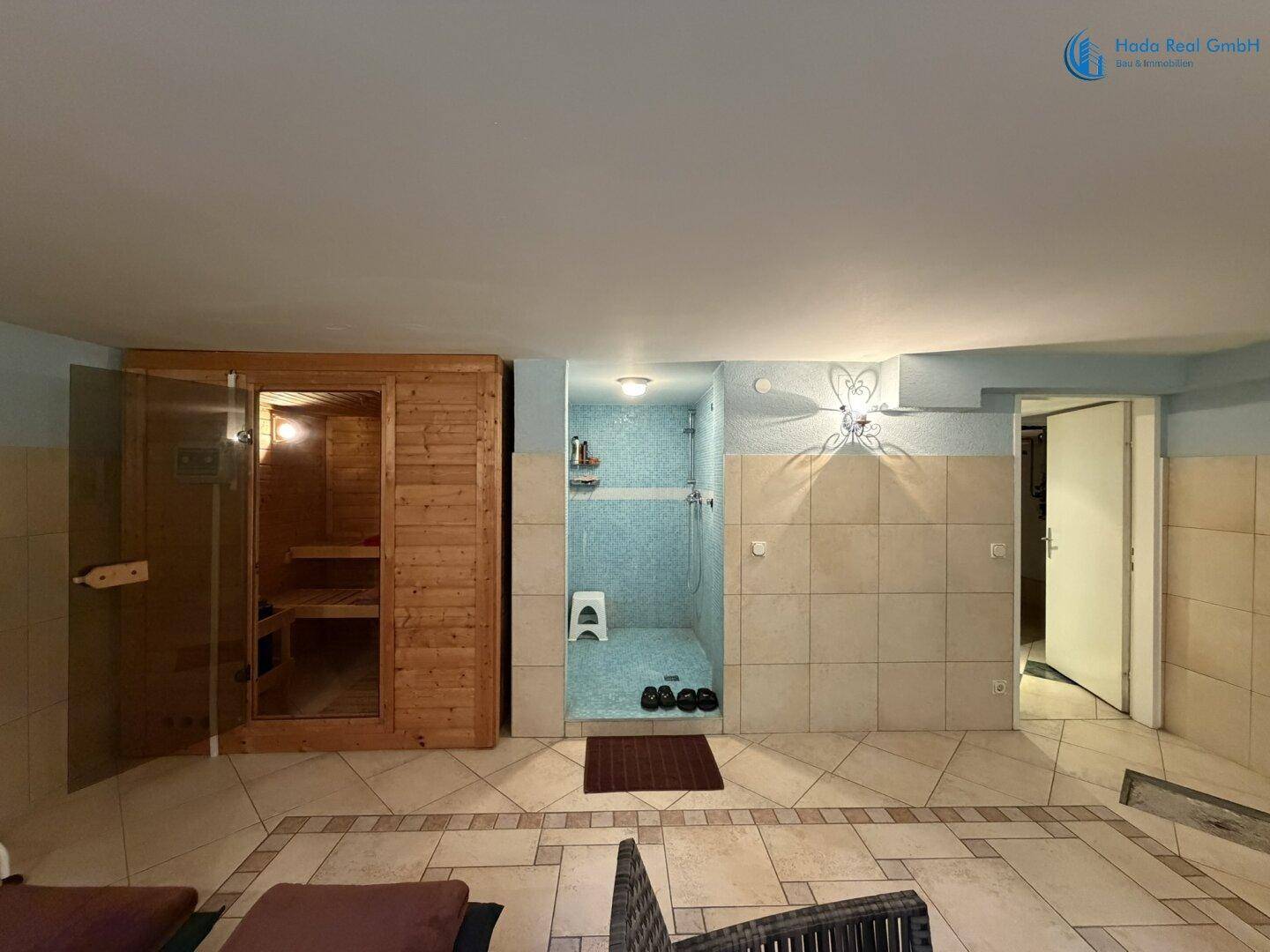 Geräumiger Wellnessbereich mit offener Sauna, Duschkabine und Fliesenboden.